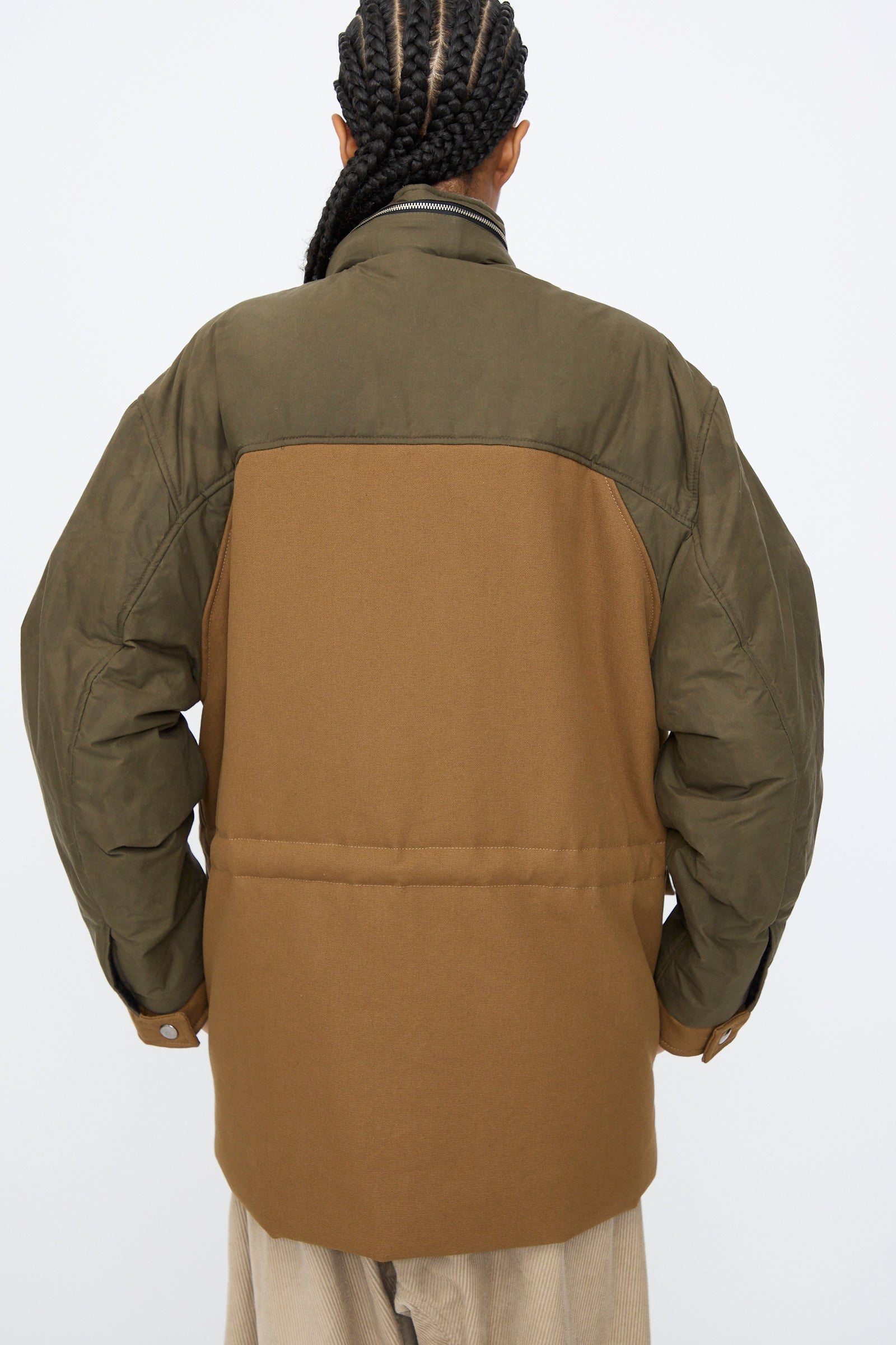 Person with braided hair wearing the Kassl Canvas Wax Field Jacket in Almond and Oil Black, photographed from the back against a plain white background.