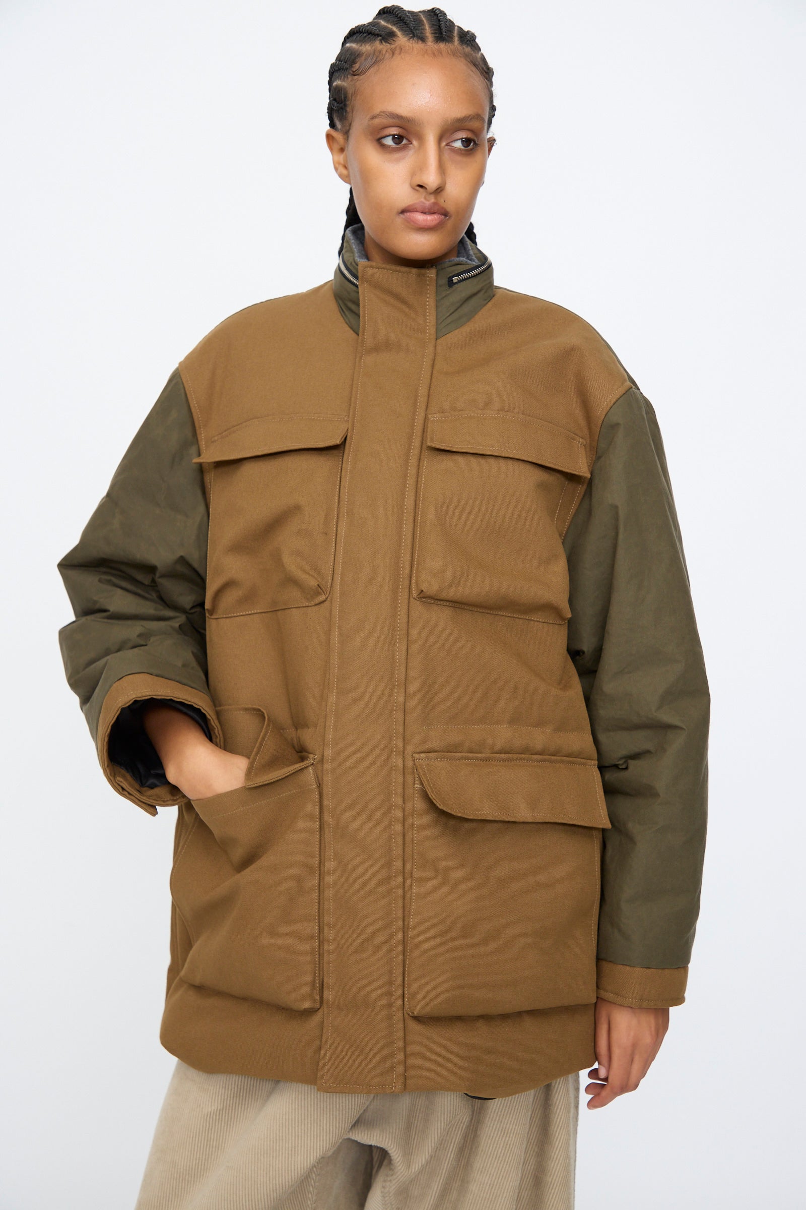 A person wears the Kassl Canvas Wax Field Jacket in Almond and Oil Black, featuring front pockets, against a plain light background.