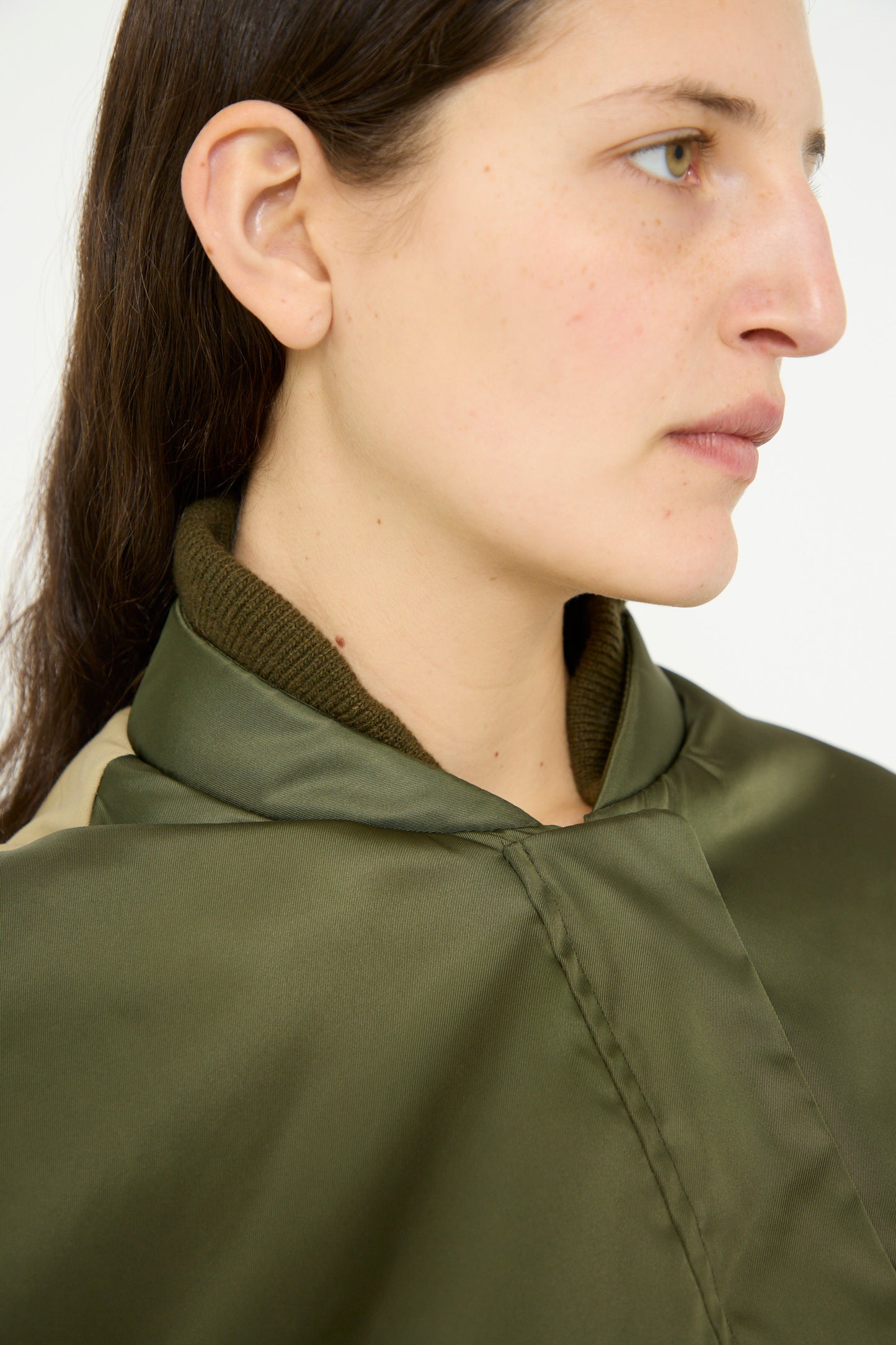 A side profile of a person with long brown hair showcases Kassl's Nylon Bomber Short in Khaki and Trench Beige, featuring an adjustable waist, set against a plain background.