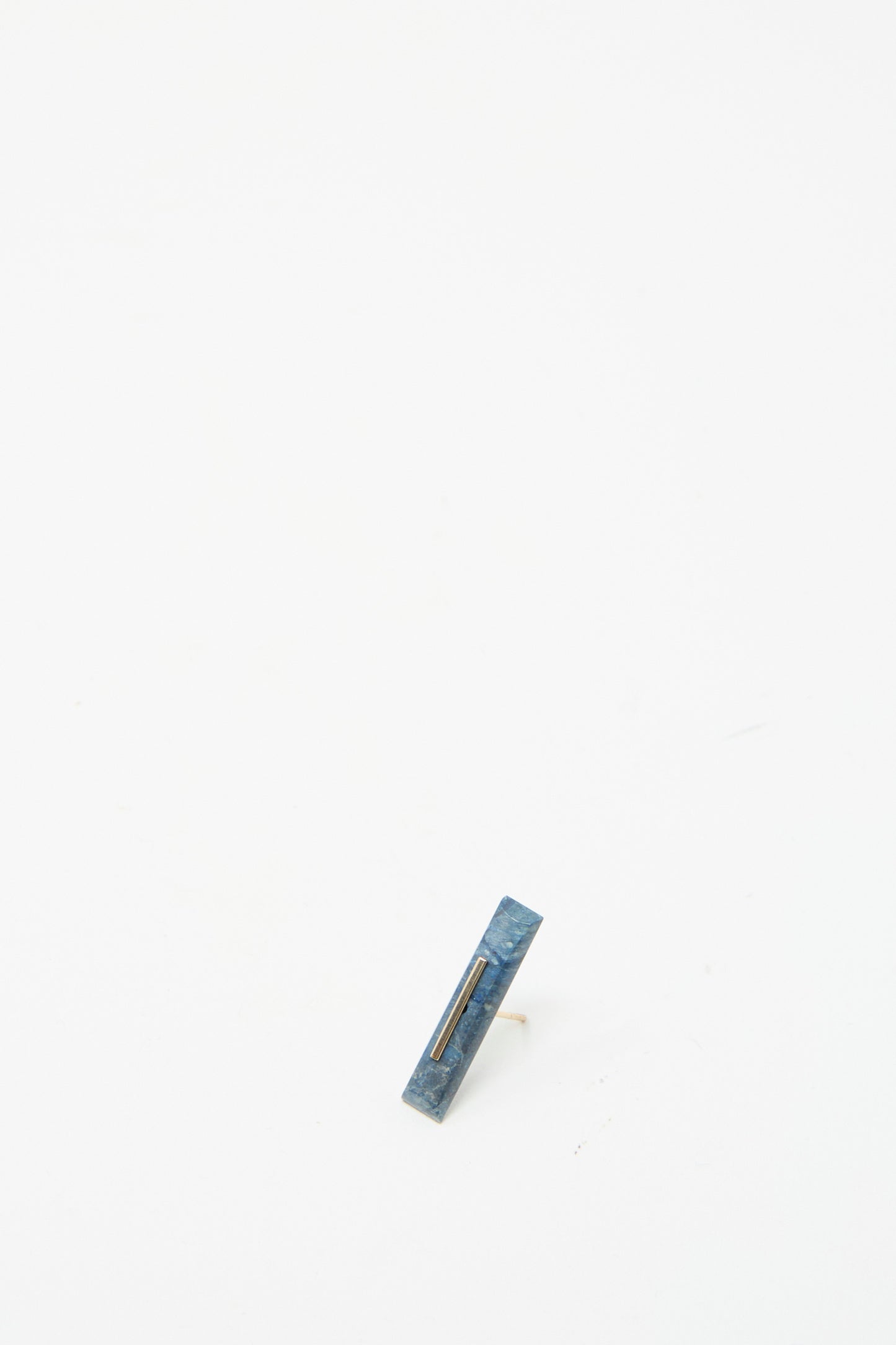 A 5mm Lapis-colored stud by Kathleen Whitaker, with a minimalist design in 14K yellow gold, stands upright against a plain white background.