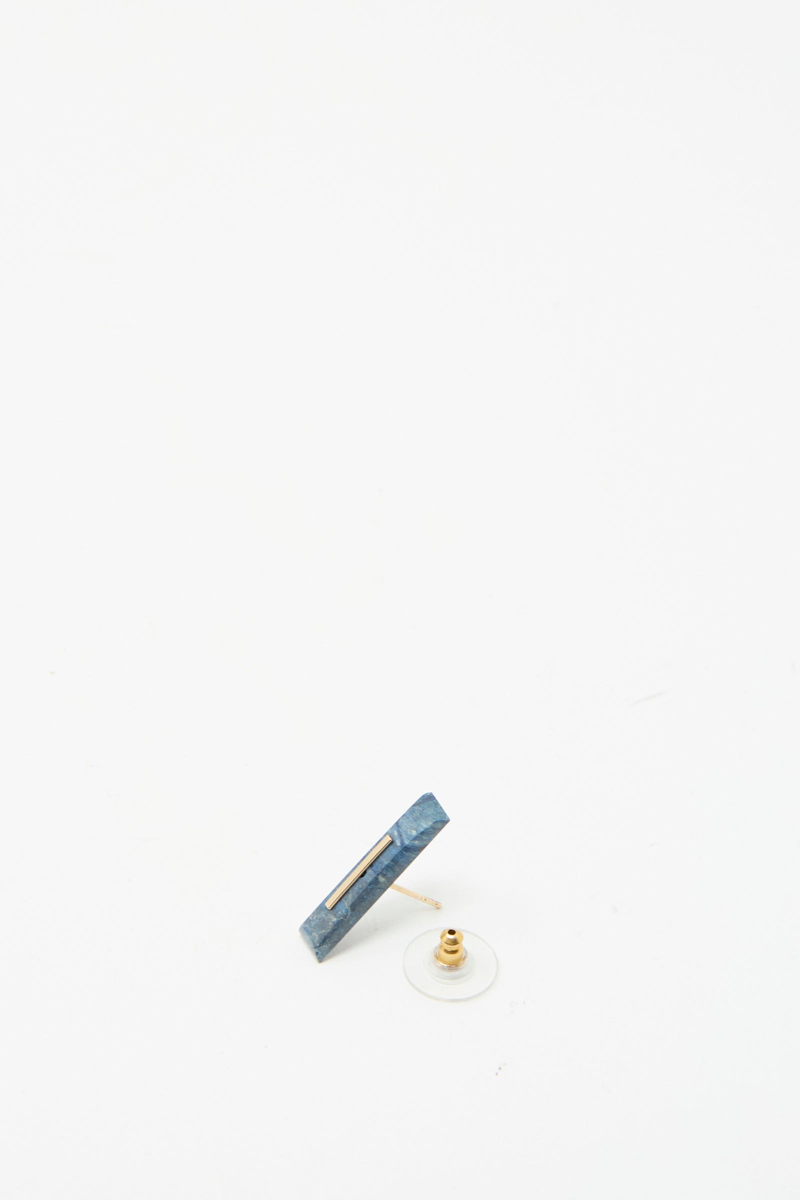 The Kathleen Whitaker 14K Yellow Gold Long Staple Stud 5mm in Lapis showcases a striking rectangular Lapis stone with a clear backing, elegantly resting on a white surface.