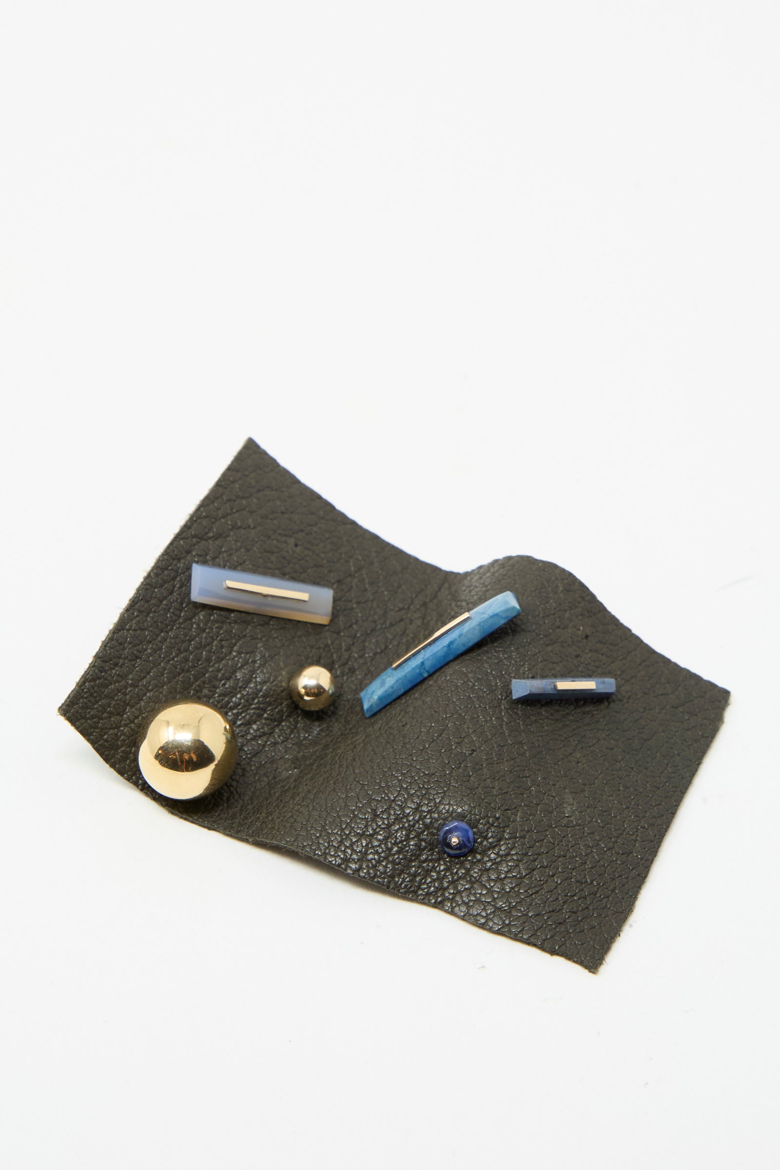 A textile featuring metallic and blue embellishments, highlighted by vintage sapphire stones, evokes the elegance of Kathleen Whitaker's 14K Yellow Gold Sapphire Stud from the brand's collection.