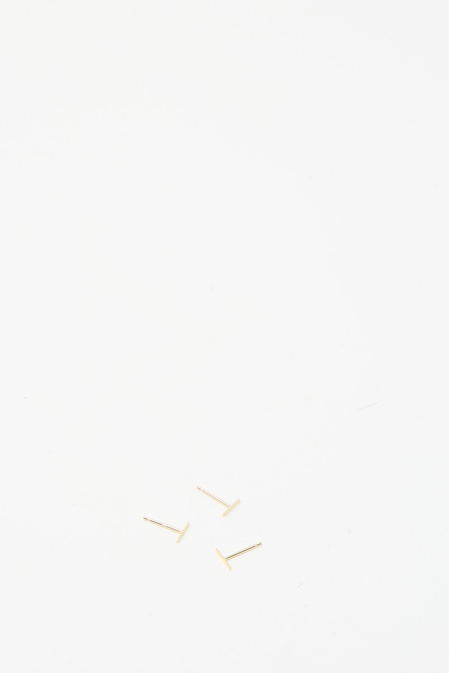 Three small screws on a plain white surface evoke the delicate craftsmanship of the 14K Yellow Gold Staple Short Stud 1/4" by Kathleen Whitaker.