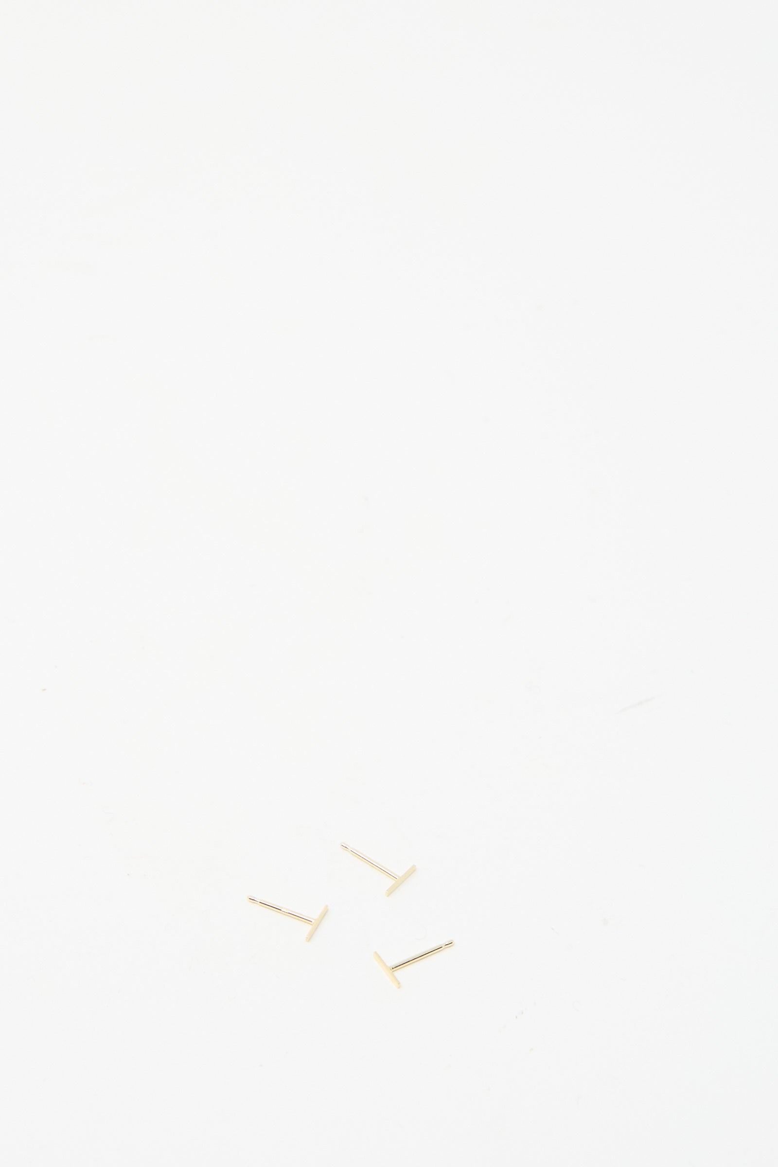 Three small screws on a plain white surface evoke the delicate craftsmanship of the 14K Yellow Gold Staple Short Stud 1/4" by Kathleen Whitaker.