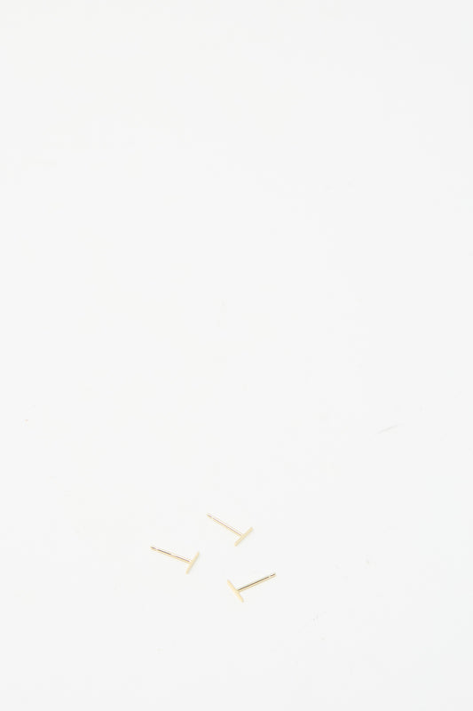 Three small earrings on a plain white surface display the delicate craftsmanship of the 14K Yellow Gold Staple Short Stud 1/4" by Kathleen Whitaker.