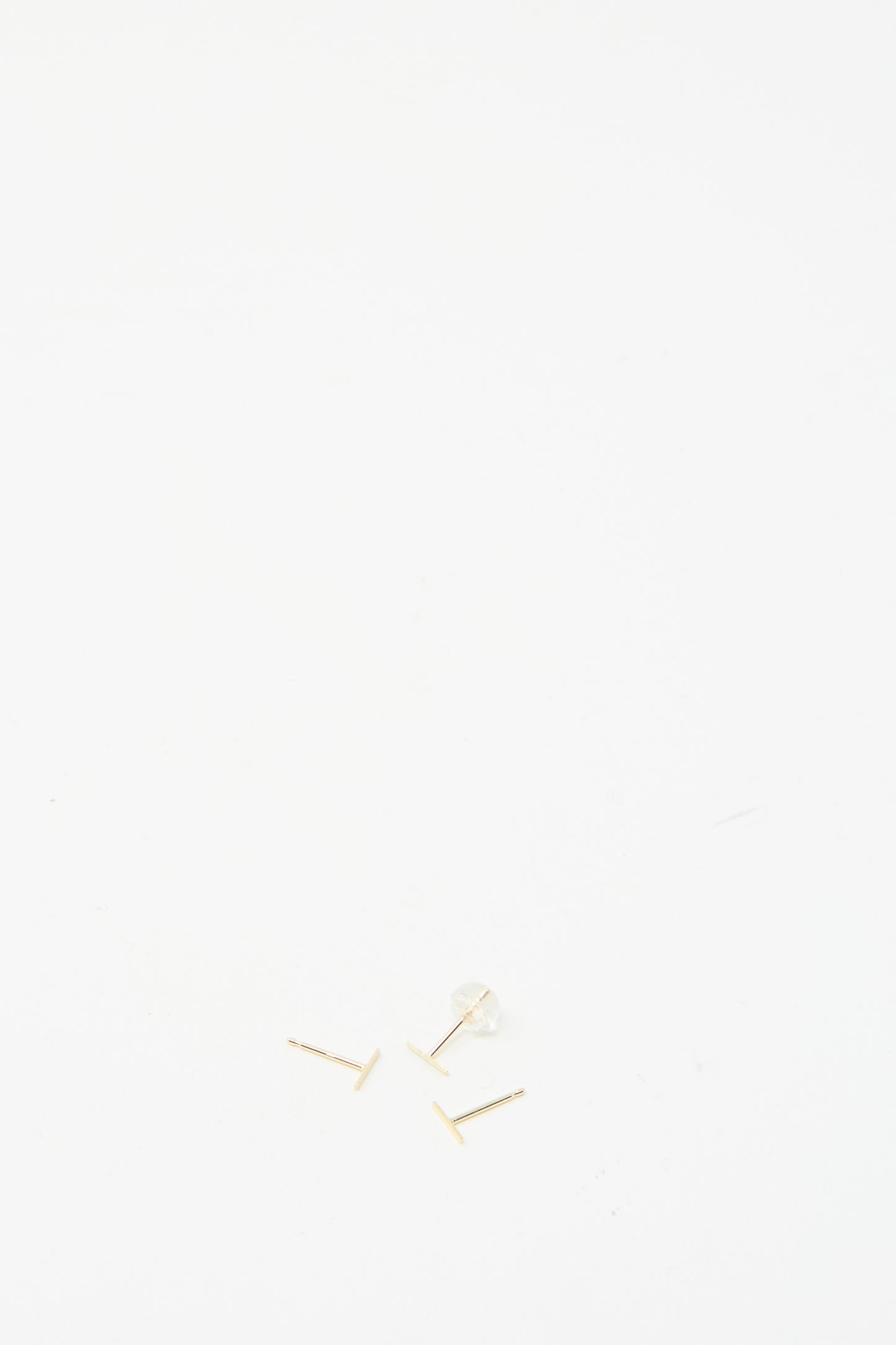 A pair of Kathleen Whitaker's 14K Yellow Gold Staple Short Stud 1/4" earrings with clear backs on a plain white backdrop.