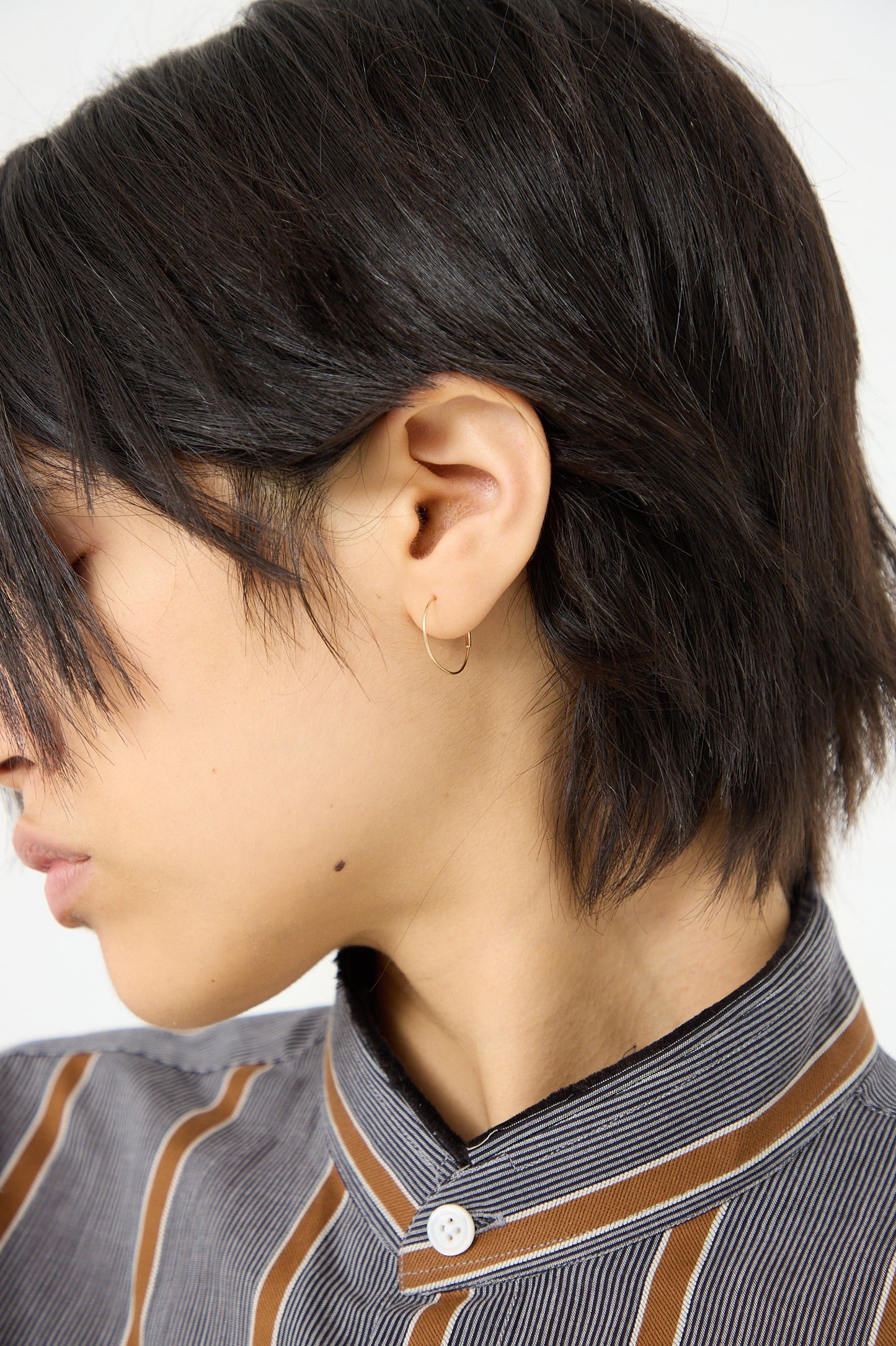 A woman wearing a striped shirt and a pair of Kathleen Whitaker hoop earrings featuring a small tube closure.