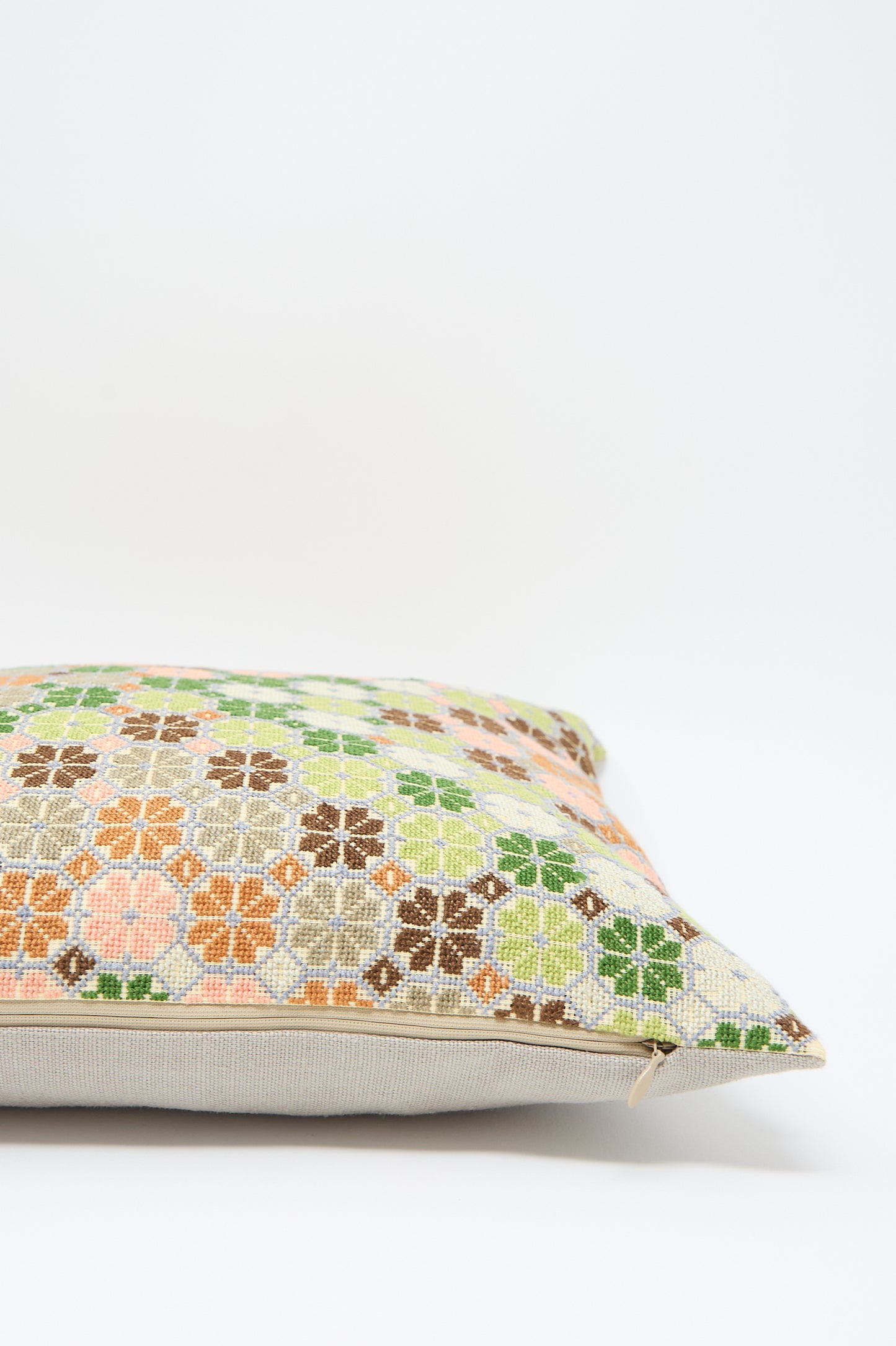 The Damask Rose Hand Embroidered Pillow in Coral and Olive by Kissweh is a one-of-a-kind pillow with a beige-edge cover featuring a colorful, intricate floral pattern in green, orange, and brown hues, placed on a white background. This exquisite piece is enhanced with geometric hand embroidery.