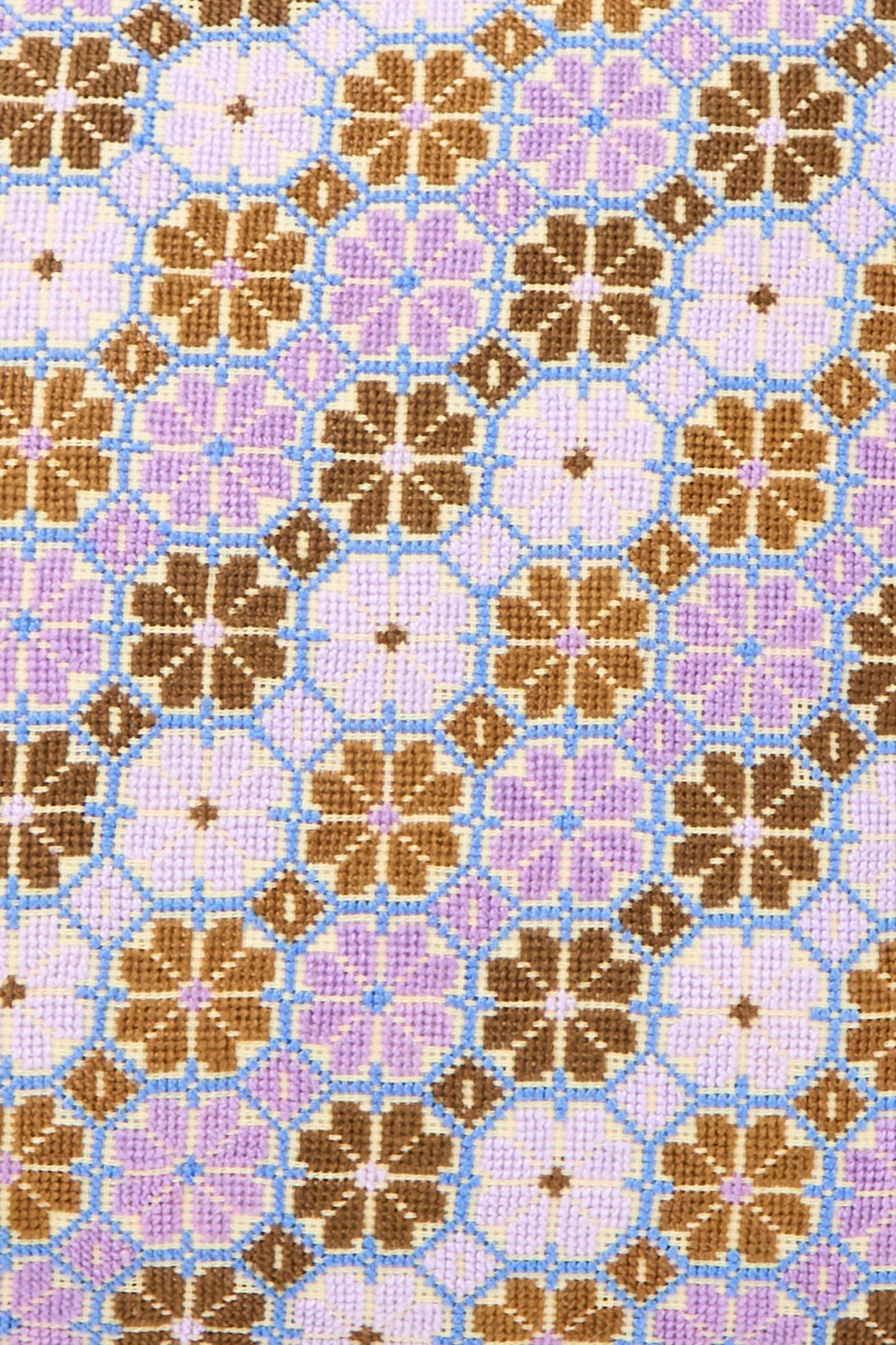 The Damask Rose Hand Embroidered Pillow in Lilac and Cognac by Kissweh features a geometric floral pattern on Libeco Belgian linen, with brown and purple blooms linked by blue lines, reminiscent of cross-stitch embroidery.