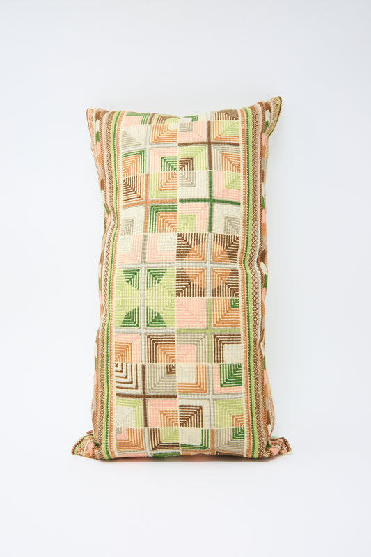 A Kissweh Double Feather Embroidered Pillow in Coral and Olive with green, pink, and orange geometric hand embroidery on a beige background, placed against a plain white backdrop.