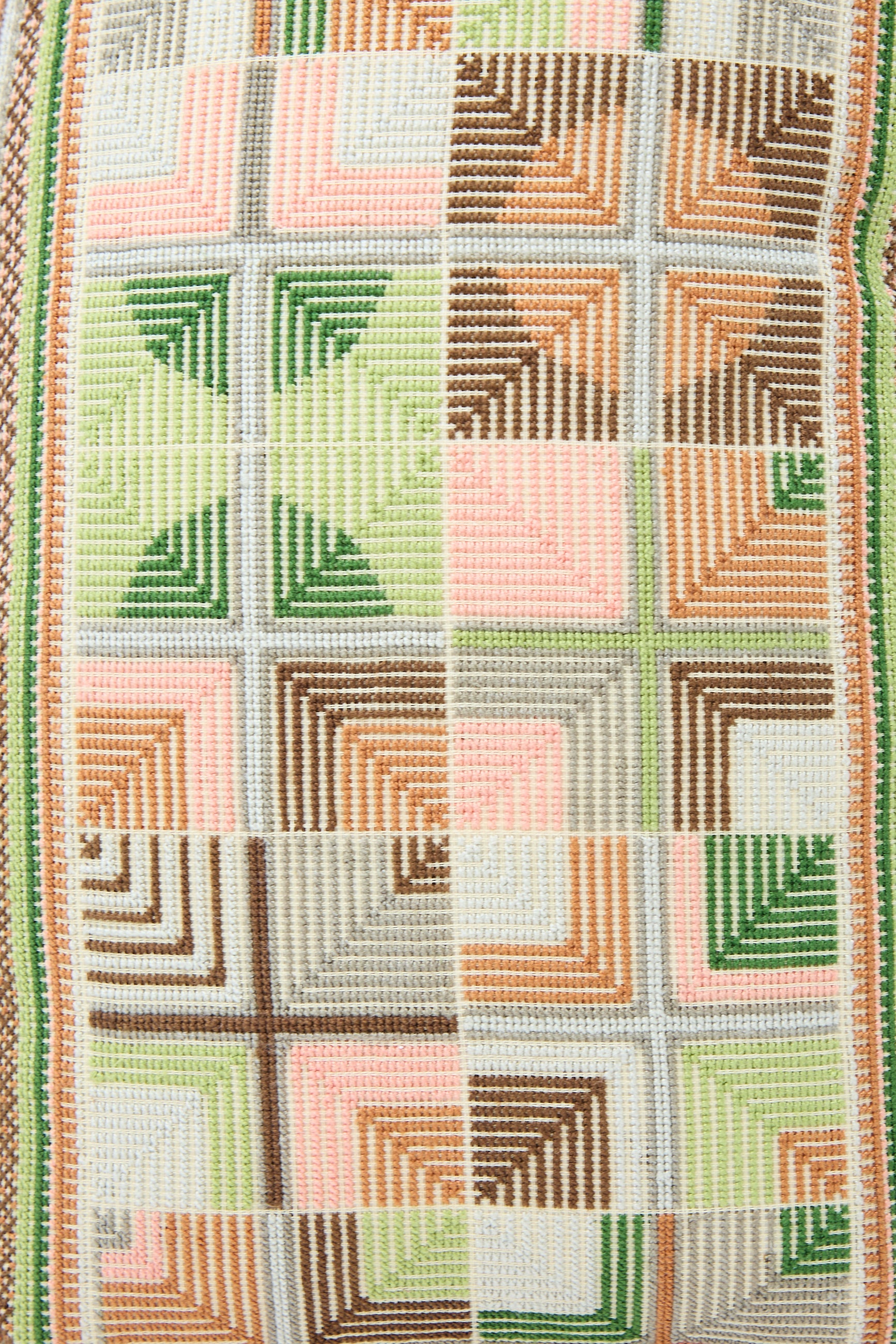 Close-up of a colorful geometric woven pattern with squares and triangles in shades of green, pink, brown, and beige on a Kissweh Double Feather Embroidered Pillow in Coral and Olive.