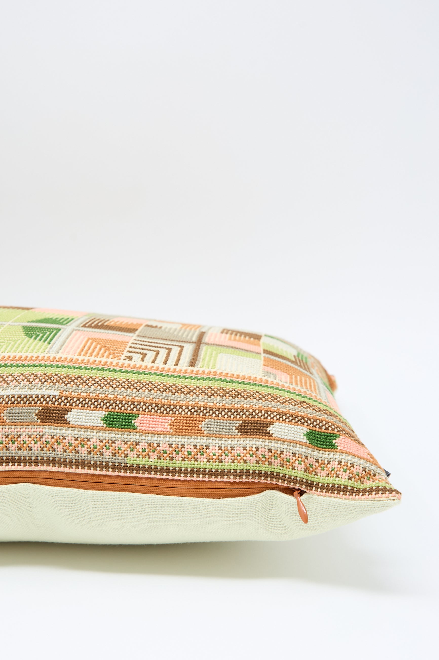 A close-up side view of the Double Feather Embroidered Pillow in Coral and Olive by Kissweh, made of Belgian linen, featuring a colorful, geometric pattern with intricate hand embroidery and a zipper on a plain white background.