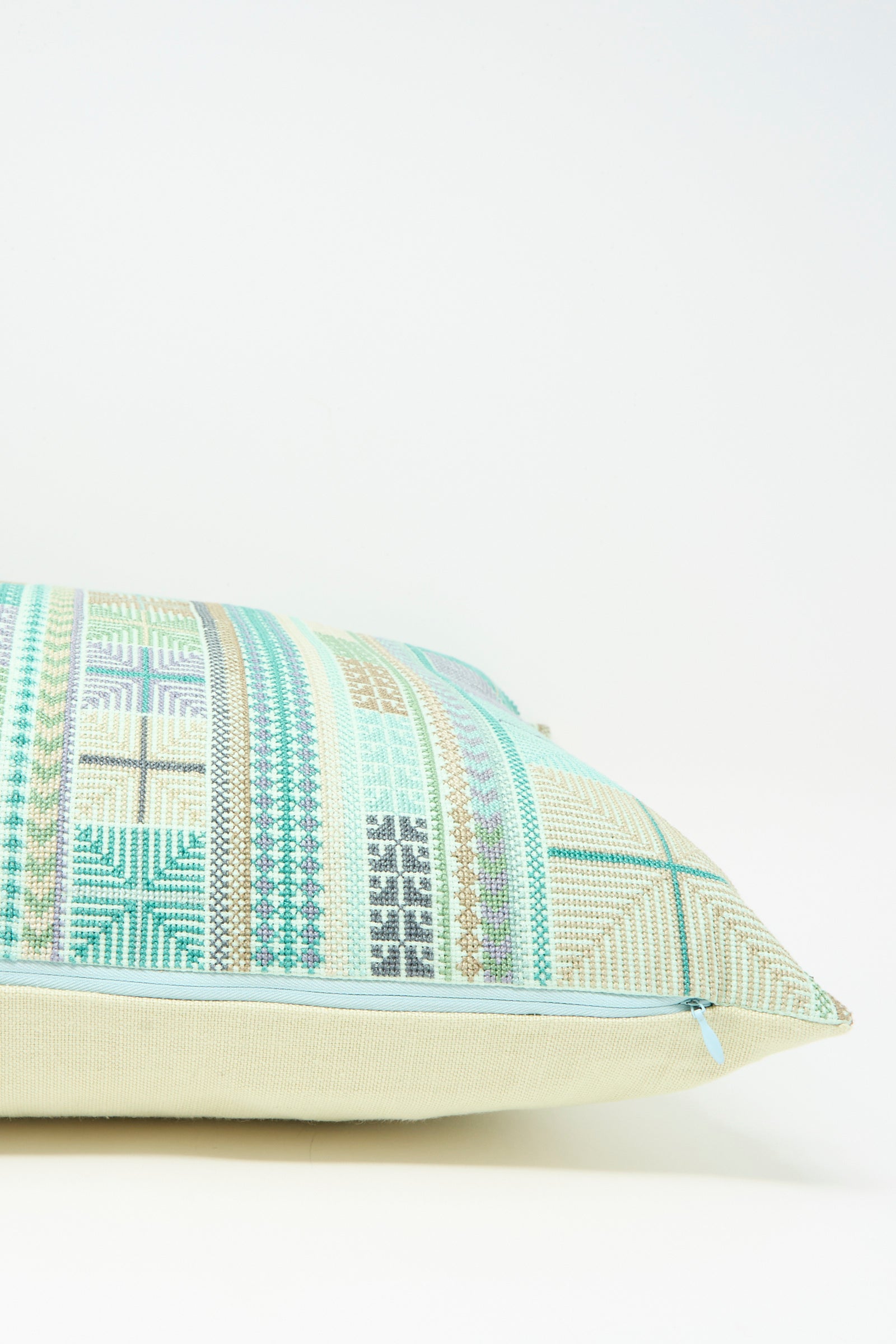 The Hanan Hand Embroidered Pillow in Acqua II by Kissweh features a geometric pattern in blue, green, and beige on Belgian linen, displayed against a plain light background.