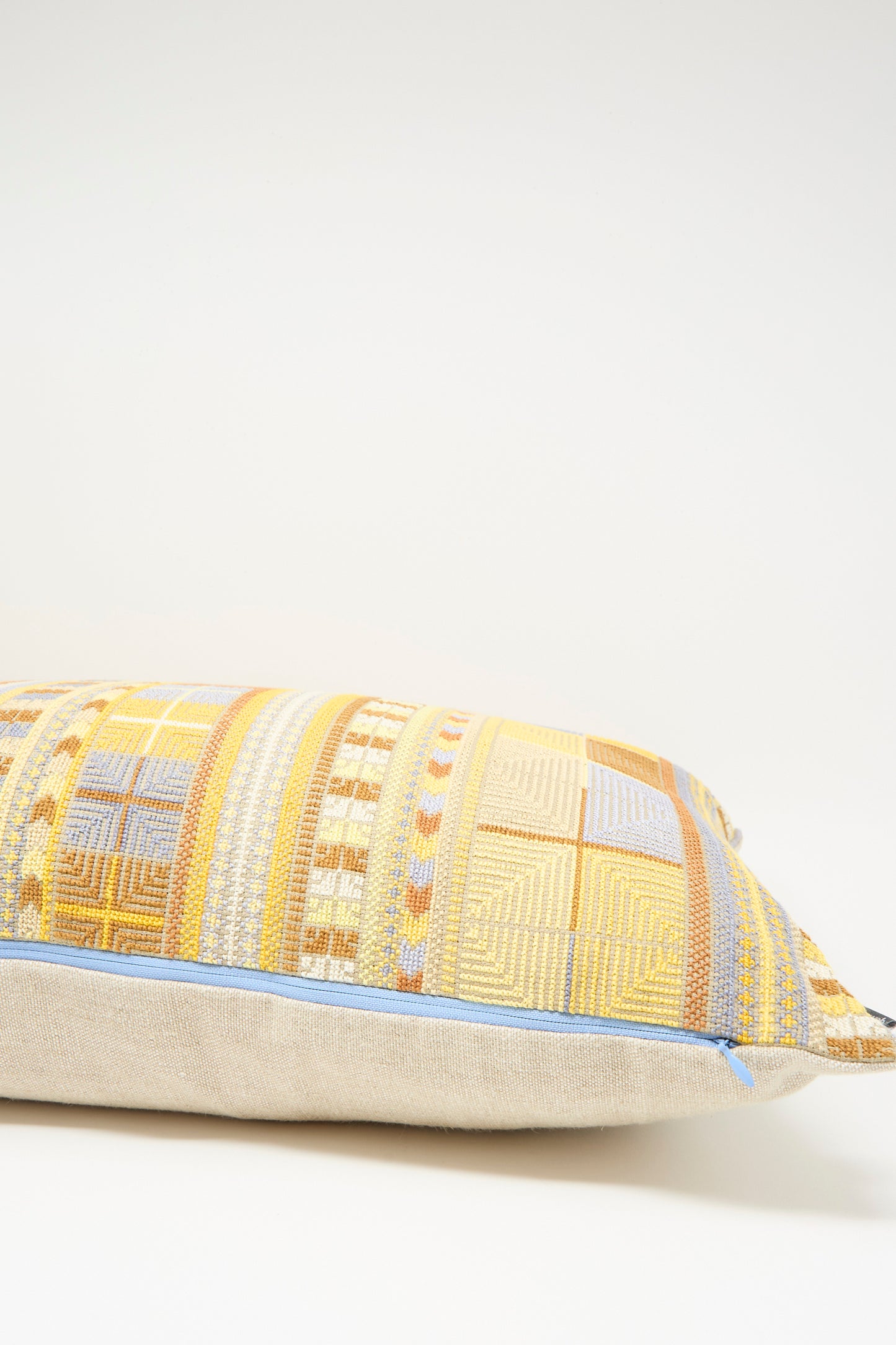 The Hanan Hand Embroidered Pillow in Mustard by Kissweh features a rectangular geometric design with textured yellow, beige, and blue embroidery, displayed against a plain light background.