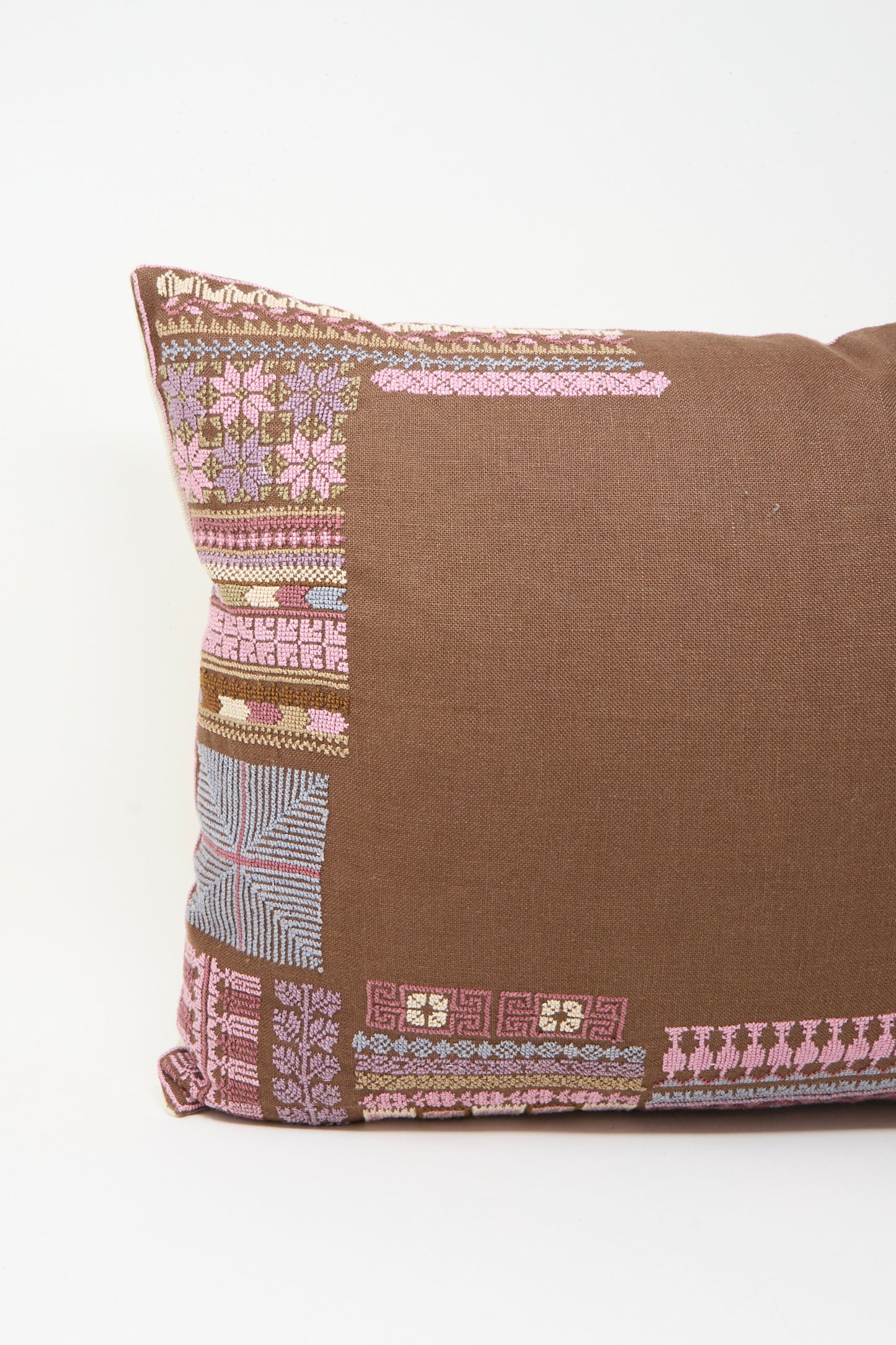 The Kissweh Imm Bushra Hand Embroidered Pillow in Chocolate features pink, lavender, and blue geometric embroidery on the left side and comes with a plush down feather insert for extra comfort. Shown against a plain white background.