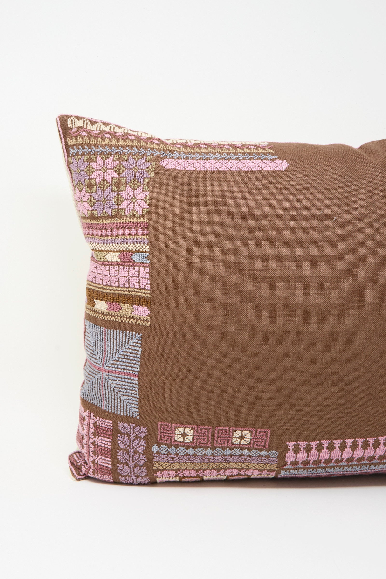 The Kissweh Imm Bushra Hand Embroidered Pillow in Chocolate features pink, lavender, and blue geometric embroidery on the left side and comes with a plush down feather insert for extra comfort. Shown against a plain white background.
