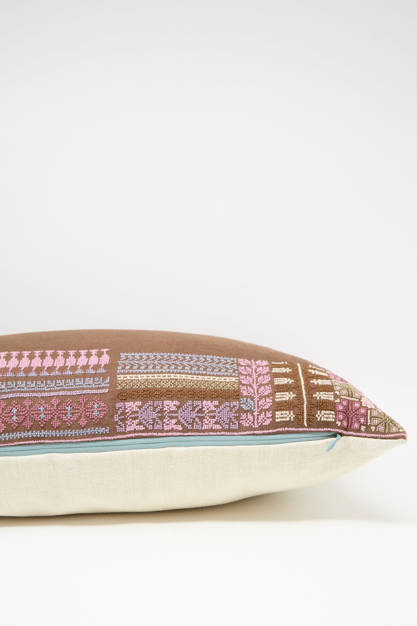 The Kissweh Imm Bushra Hand Embroidered Pillow in Chocolate features pink and blue geometric designs and a down feather insert, displayed on a white surface.