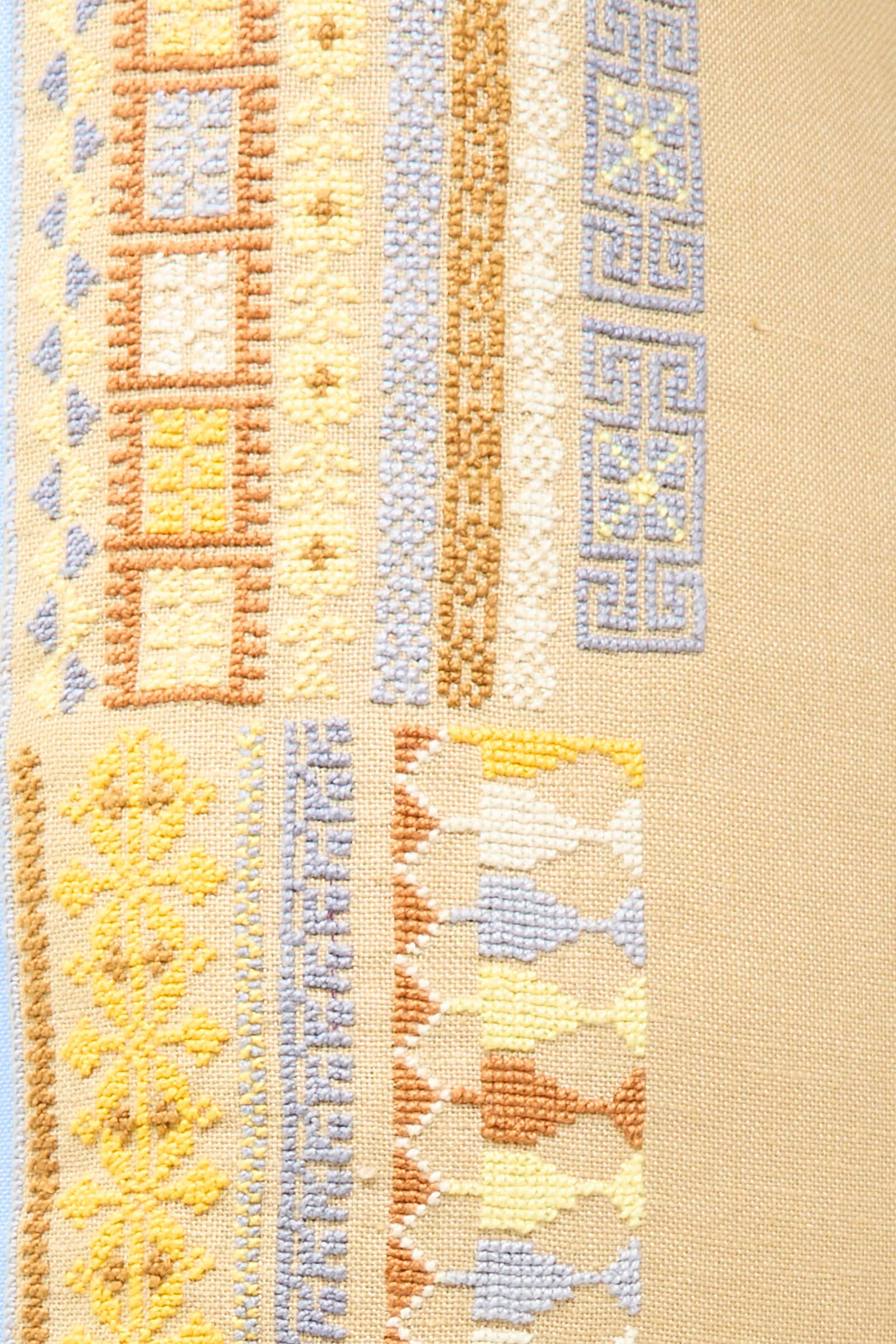 Close-up of the Kissweh Imm Bushra Hand Embroidered Pillow in Mustard, featuring beige Belgian linen with hand-embroidered geometric patterns in blue, yellow, white, and brown thread across rows of various shapes.