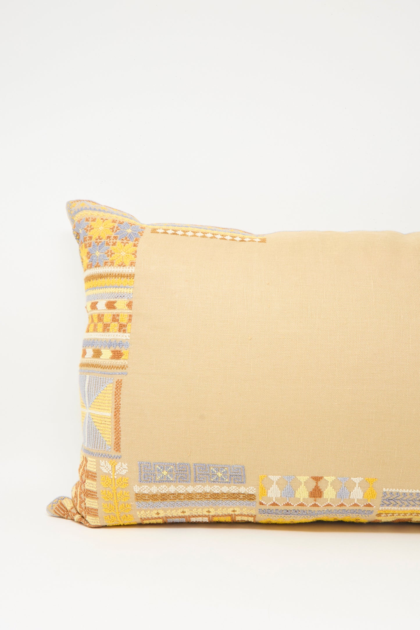The Kissweh Imm Bushra Hand Embroidered Pillow in Mustard is a rectangular Belgian linen pillow with multicolored geometric corner patterns, shown against a plain white background.