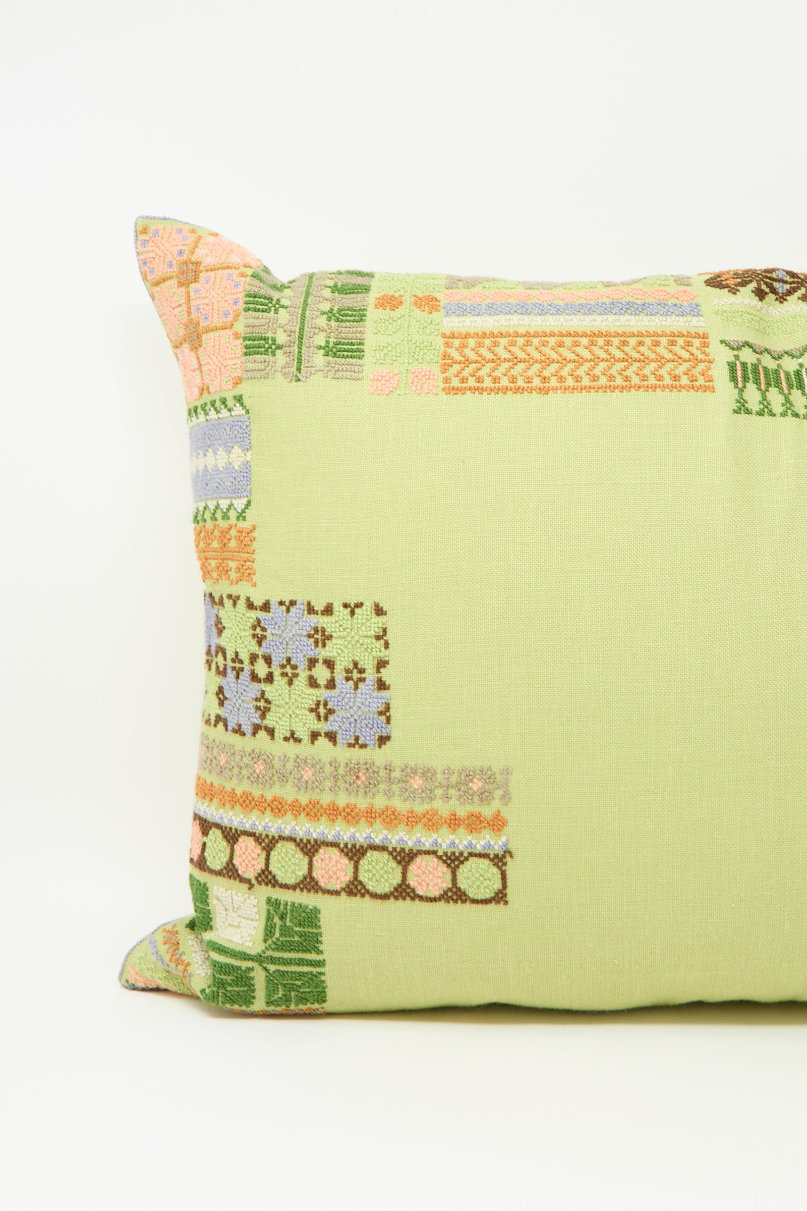 The Imm Bushra Hand Embroidered Pillow in Olive by Kissweh features multicolored geometric embroidery on light green Belgian linen, with a plush down feather insert for comfort.