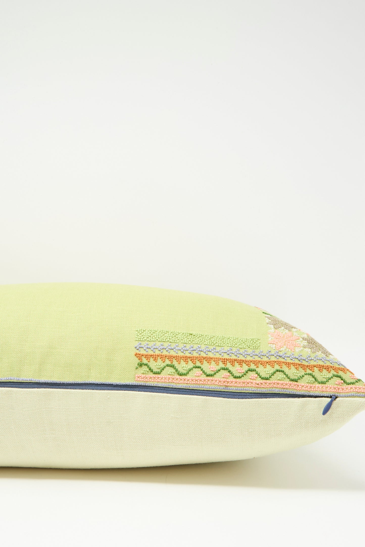 The Imm Bushra Hand Embroidered Pillow in Olive by Kissweh features decorative embroidery on a light green and beige Belgian linen cover with blue piping, plus a plush down feather insert, shown on a white background.