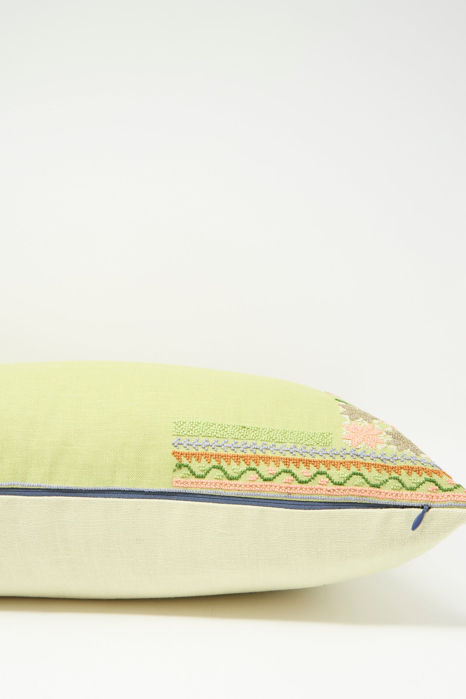 The Imm Bushra Hand Embroidered Pillow in Olive by Kissweh features decorative embroidery on a light green and beige Belgian linen cover with blue piping, plus a plush down feather insert, shown on a white background.