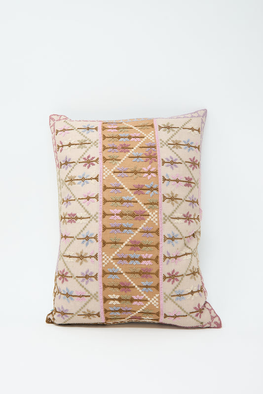 A Kissweh Imm Omar Hand Embroidered Pillow in Beige and Cognac with a traditional geometric and floral pattern in shades of brown, beige, pink, and purple on a white Belgian linen background.