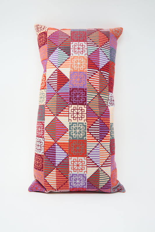 Ola Hand Embroidered Pillow in Crimson by Kissweh with a multicolored patchwork pattern, featuring red, purple, green, and beige geometric designs against a white background. Crafted from Belgian linen with intricate geometric hand embroidery for added texture and elegance.