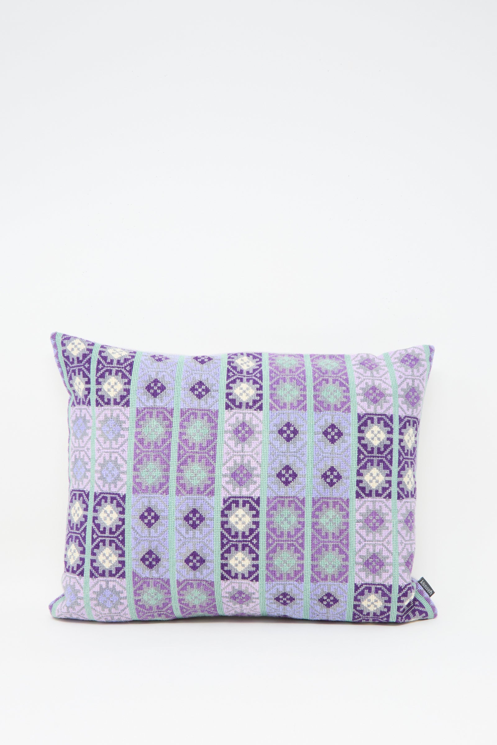 The Kissweh Wafa'a Hand Embroidered Pillow in Lilac features a rectangular shape with geometric purple, blue, and white embroidery on a crisp white background. Comes with a plush down feather insert for extra comfort.