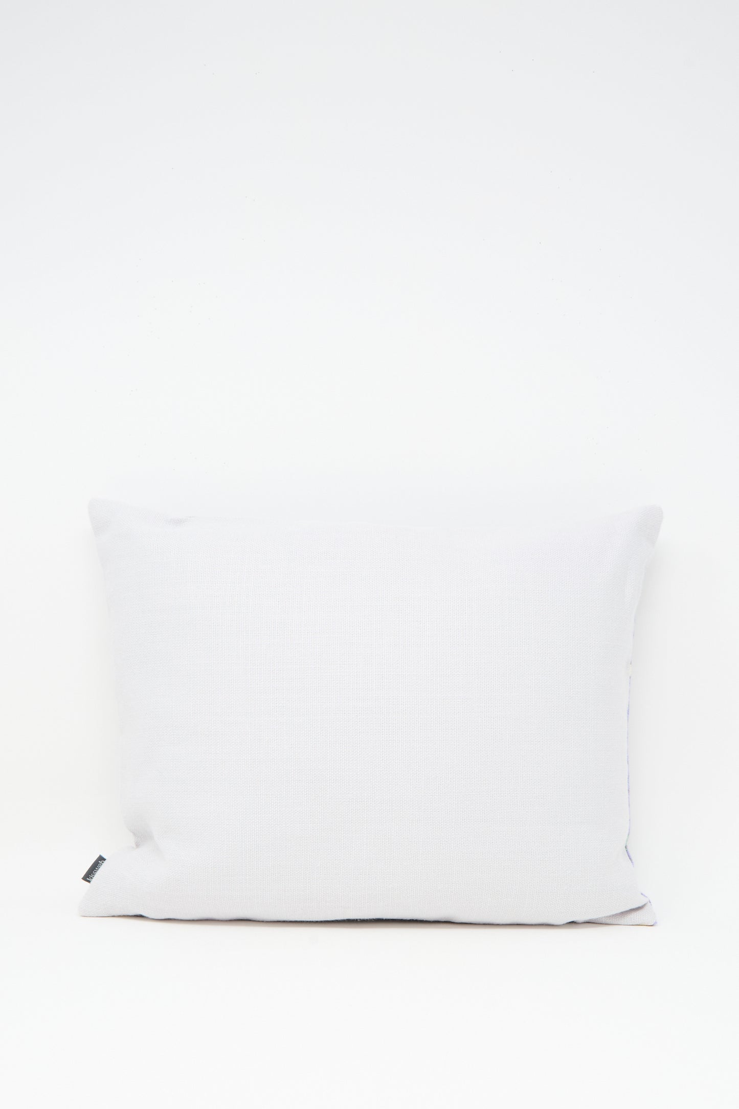 The Wafa'a Hand Embroidered Pillow in Lilac by Kissweh features intricate embroidery and a subtle lilac hue, shown here with a down feather insert and a small black tag on the left side against a white background.