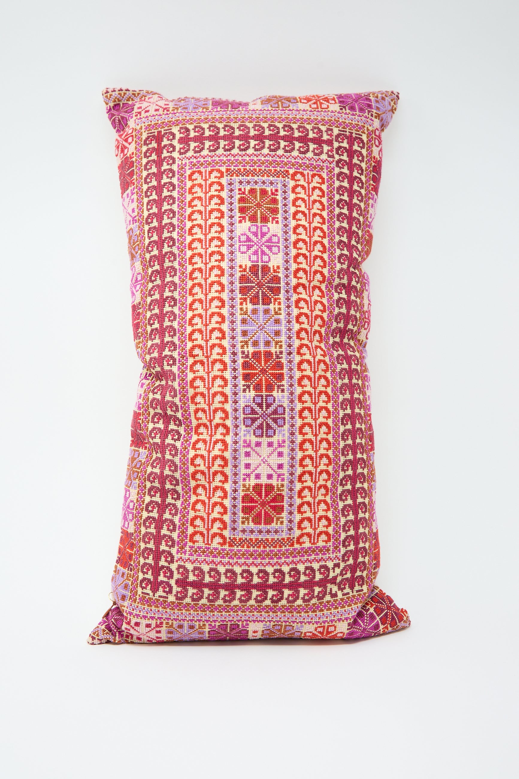 Yasmin Hand Embroidered Pillow in Crimson by Kissweh, a rectangular lumbar pillow crafted from Belgian linen, featuring a colorful, intricate geometric pattern in red, pink, and purple tones.