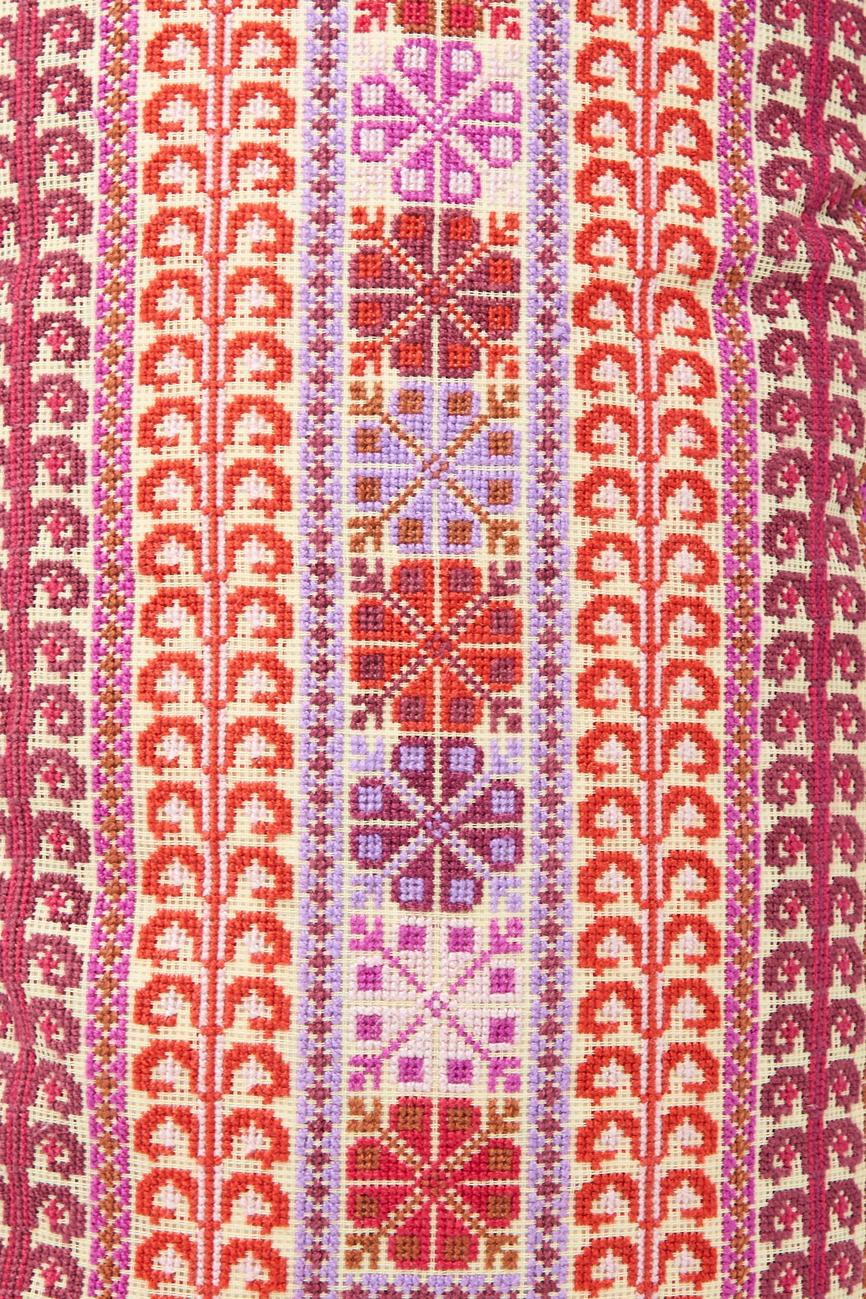 A close-up shot of a colorful textile pattern featuring vertical rows of geometric and floral designs in red, pink, and orange tones, meticulously hand embroidered on the Yasmin Hand Embroidered Pillow in Crimson by Kissweh.