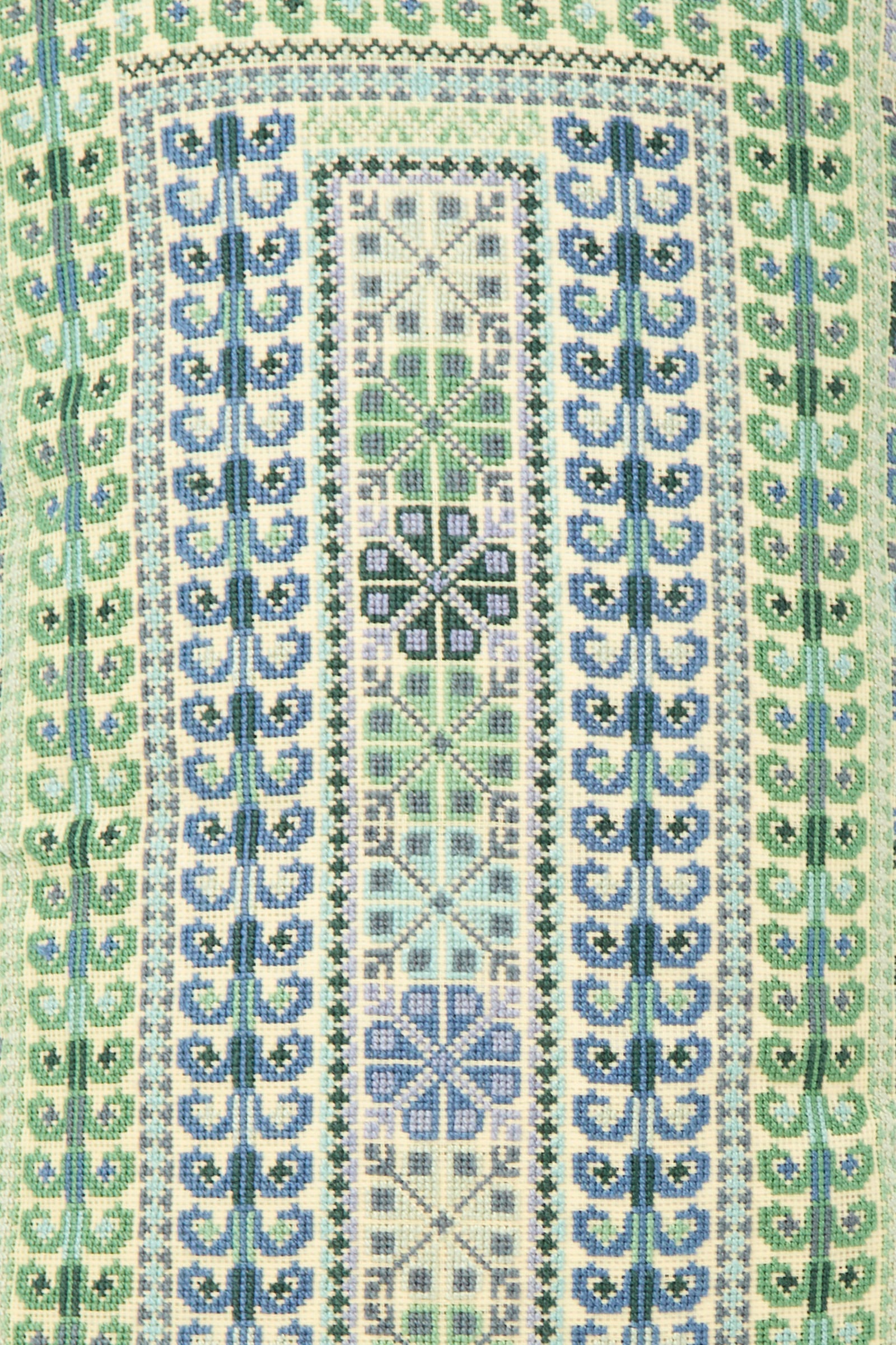 The Yasmin Hand Embroidered Pillow in Olive by Kissweh features geometric and floral patterns in blue, green, and beige on Belgian linen, arranged in vertical, symmetrical rows.