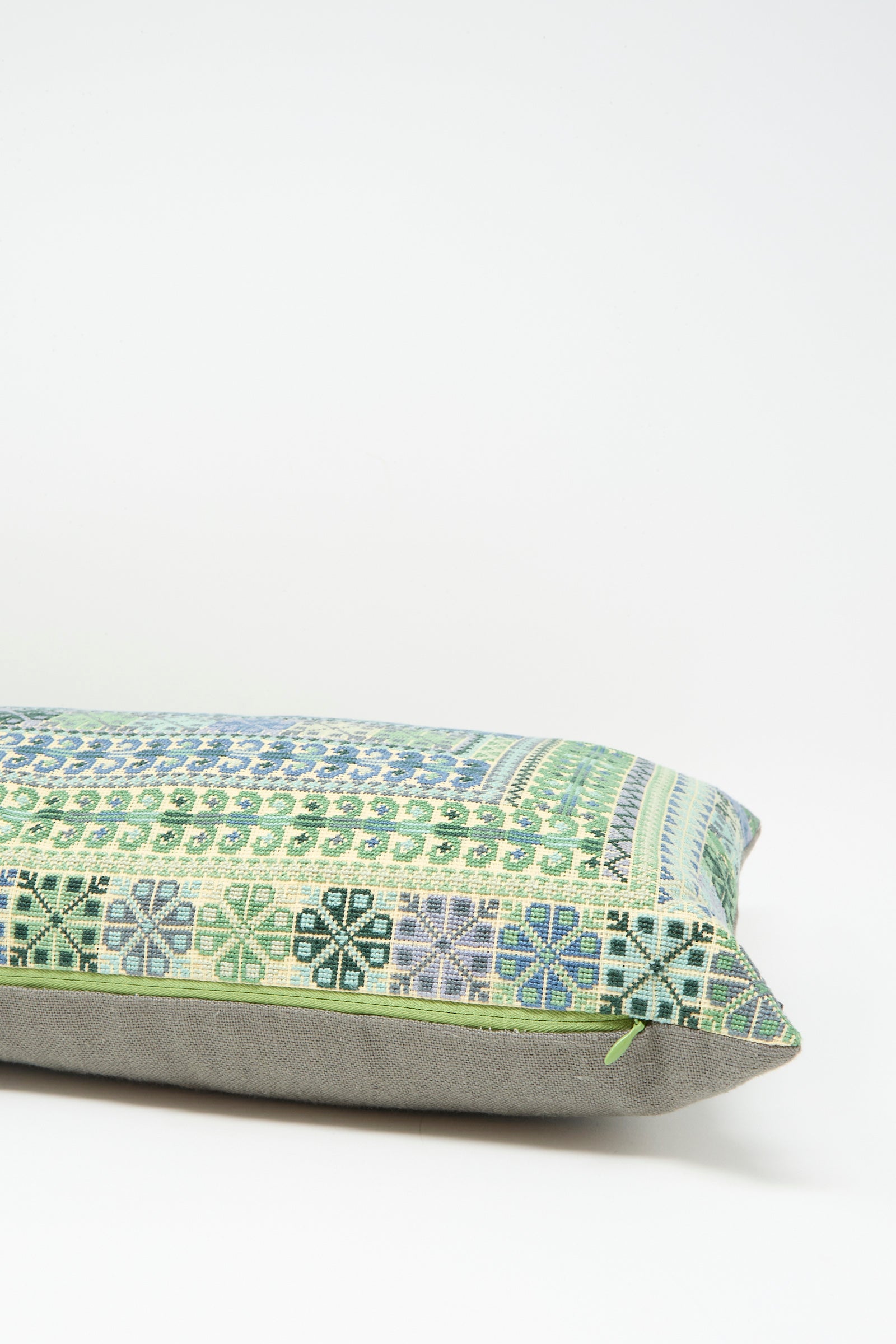 The Kissweh Yasmin Hand Embroidered Pillow in Olive features a green and blue geometric design on Belgian linen with a plain gray bottom, shown on a white background.