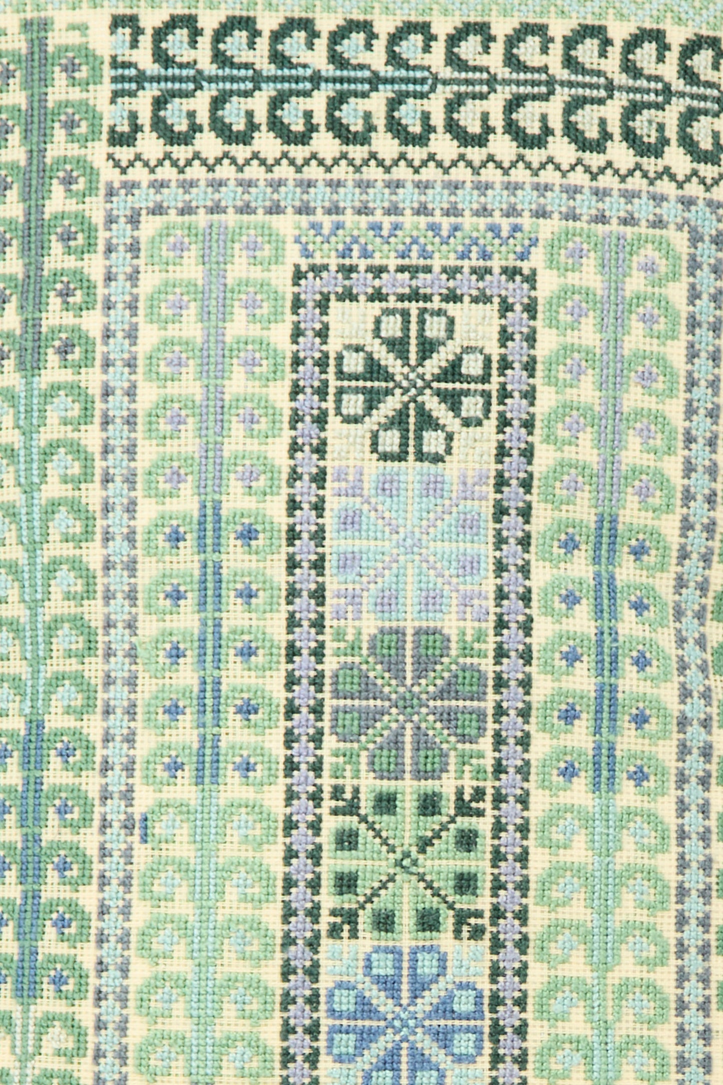 A close-up of the Yasmin Hand Embroidered Pillow in Olive and Slate by Kissweh shows intricate geometric patterns in green, blue, and purple tones—ideal for a striking lumbar accent.