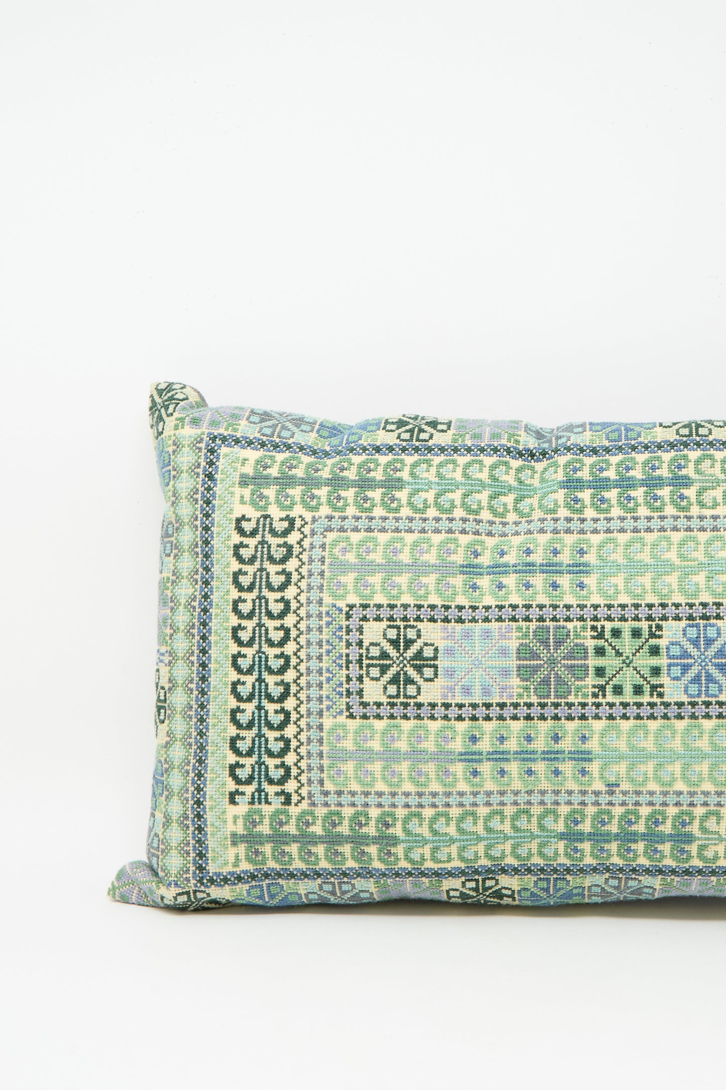 The Yasmin Hand Embroidered Pillow in Olive and Slate by Kissweh features a geometric pattern in green, blue, and beige on white Belgian linen.