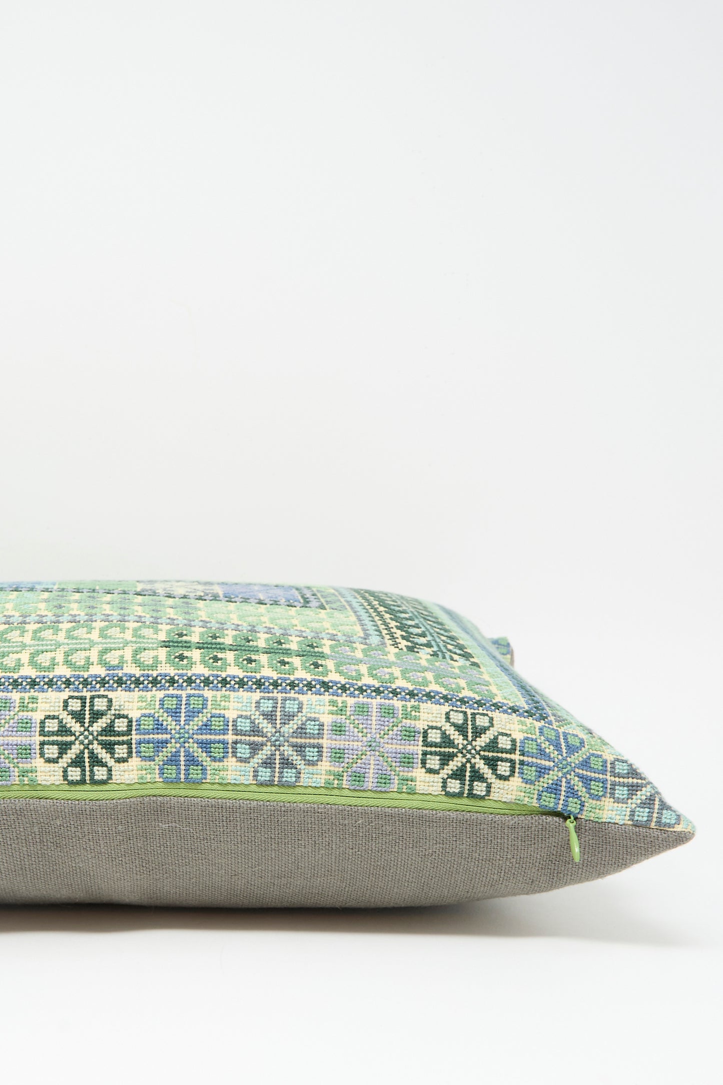 The Yasmin Hand Embroidered Pillow in Olive and Slate by Kissweh features a green, blue, and black geometric design on Belgian linen with a plain gray bottom, displayed against a white background.