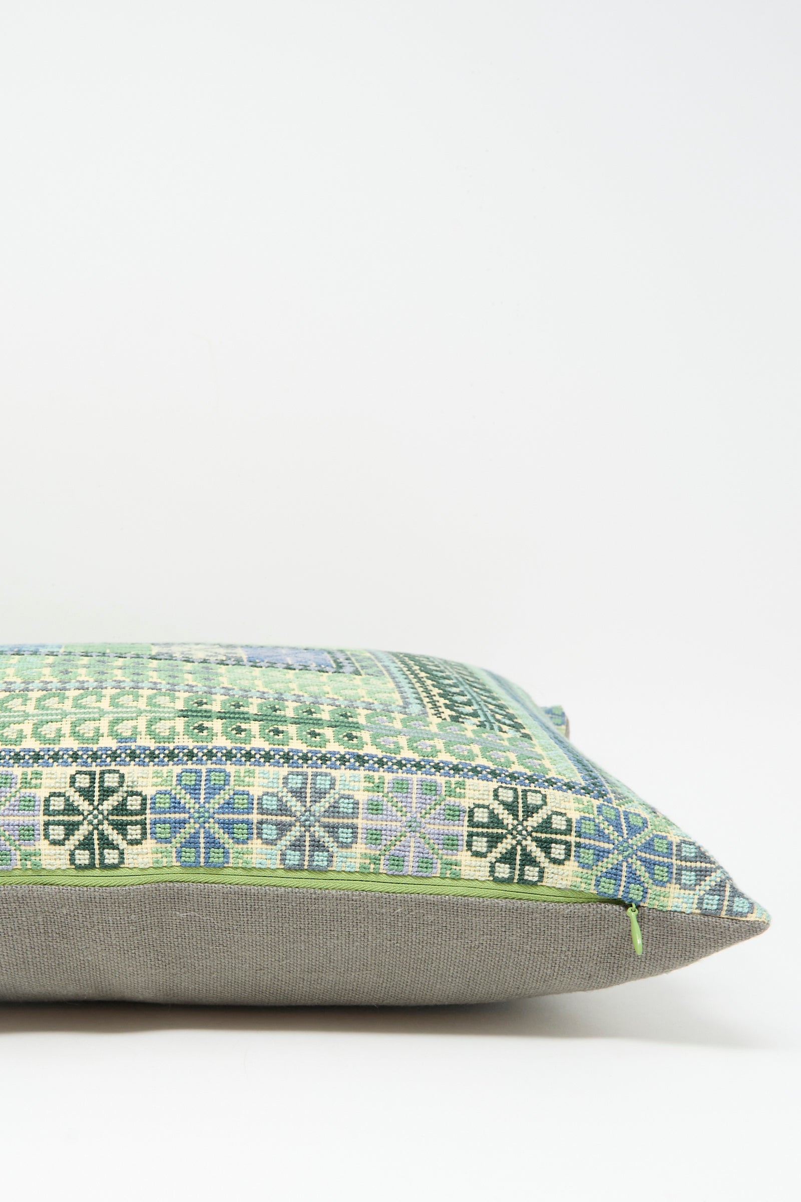 The Yasmin Hand Embroidered Pillow in Olive and Slate by Kissweh features a green, blue, and black geometric design on Belgian linen with a plain gray bottom, displayed against a white background.