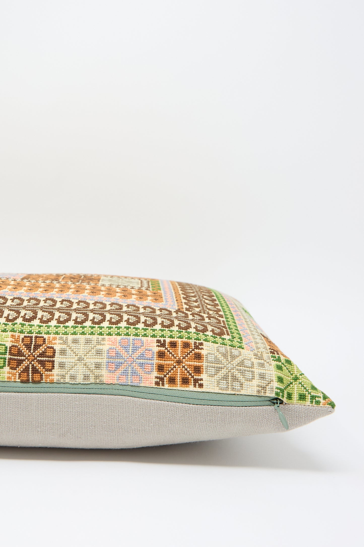 A Yasmin Hand Embroidered Pillow in Olive and Slate with a multicolored, intricate geometric hand embroidery pattern against a white background. The design includes green, brown, and pastel-colored sections, crafted from fine Belgian linen by Kissweh.