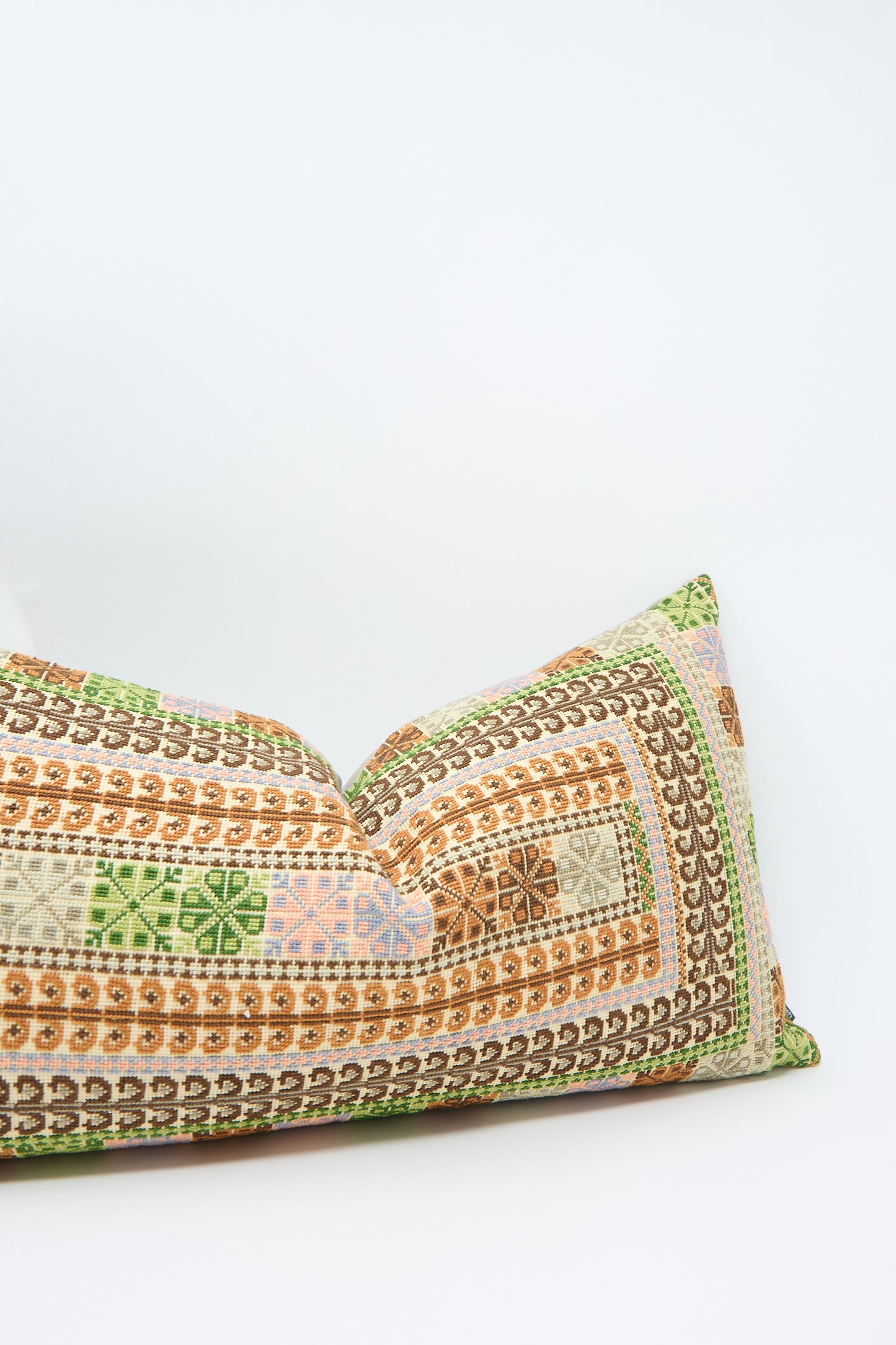 A Yasmin Hand Embroidered Pillow in Olive and Slate by Kissweh, featuring a mix of green, orange, brown, and pink geometric designs on Belgian linen, placed against a plain white background.