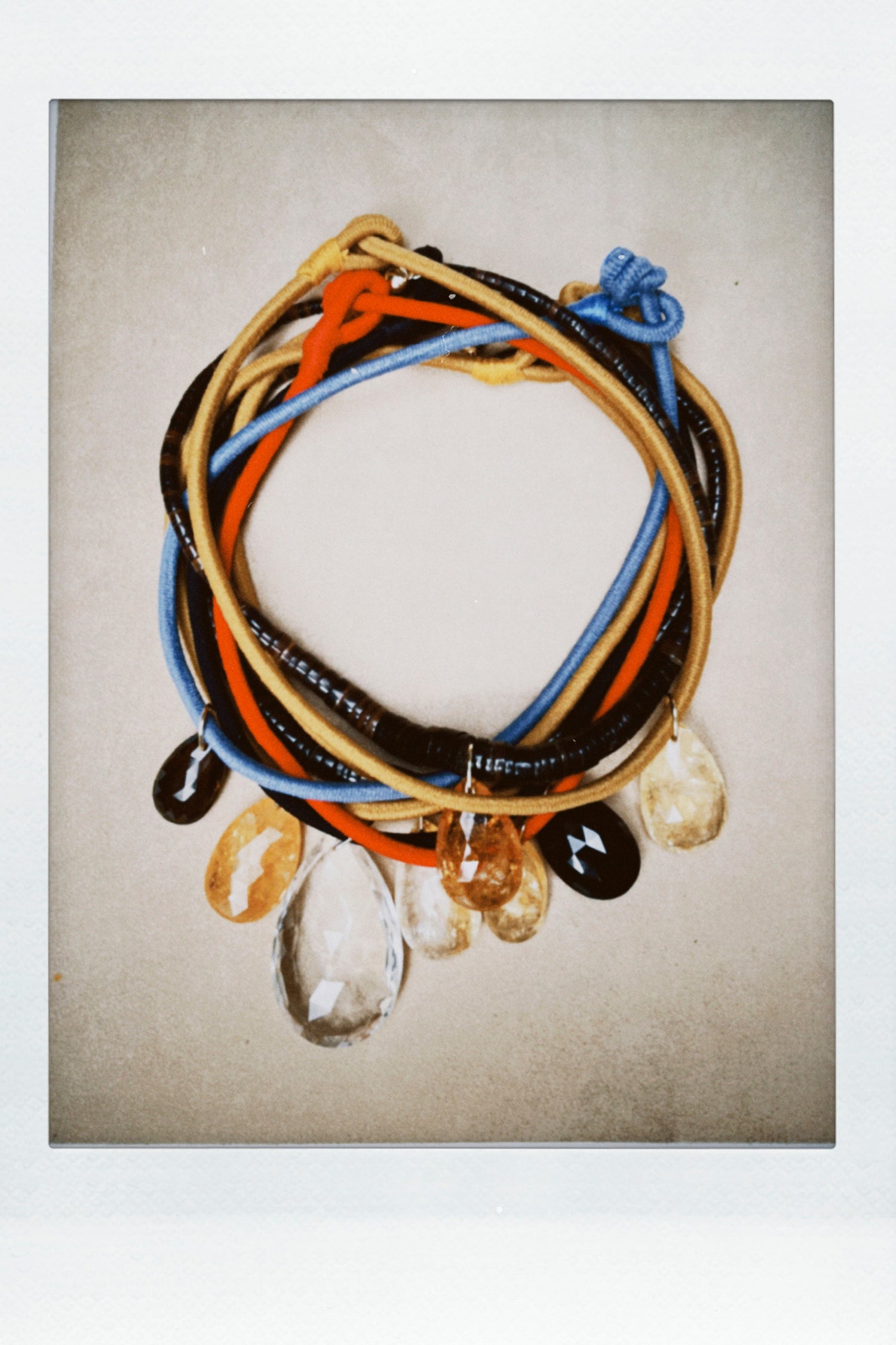 A stack of colorful cord necklaces with dangling polished stone charms from Laoli, photographed against a neutral textured background.