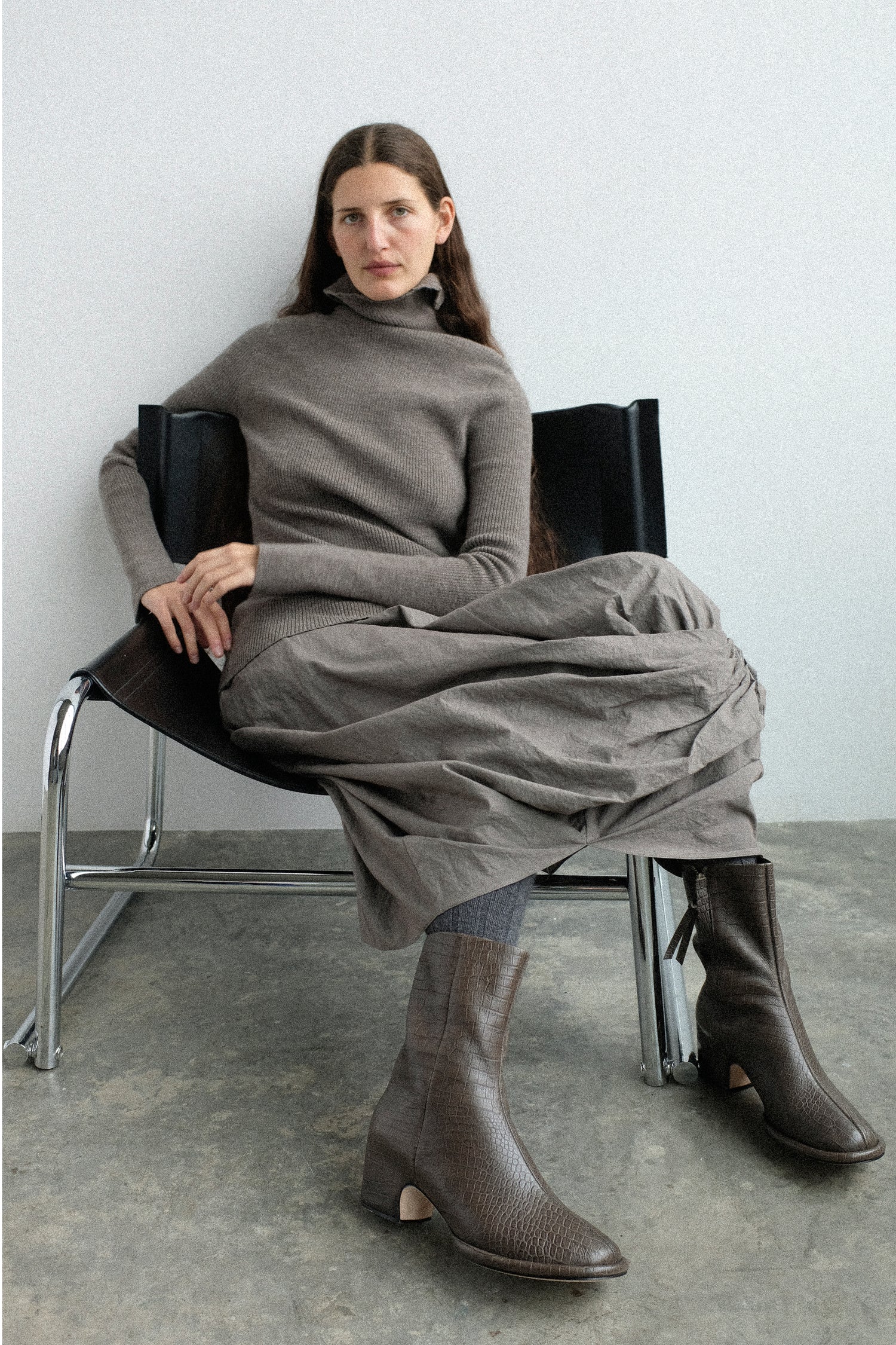 A woman sitting in a chair wearing pieces for the Lauren Manoogian FW25 collection against a black background.