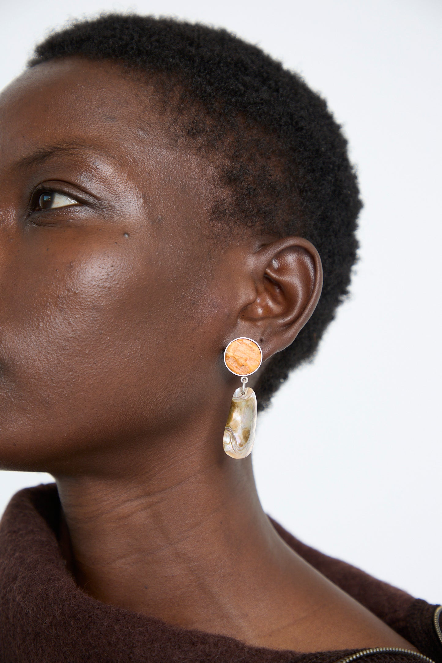 A person with the La Mar's Sterling Silver No. 09 Earrings in Orange and Shell, showcasing an orange shell and a drop with sterling silver.