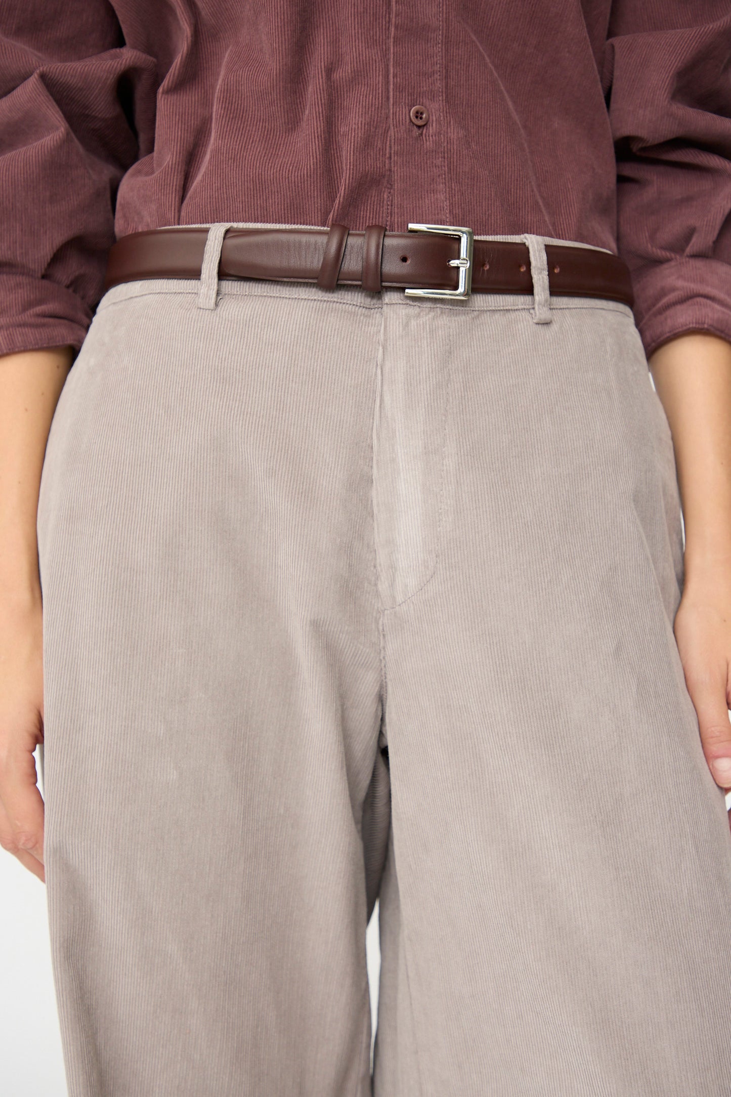 A person wearing a maroon cotton needlecord shirt tucked into Labo.Art’s Binocchio Trouser in Malva, paired with a dark brown leather belt.