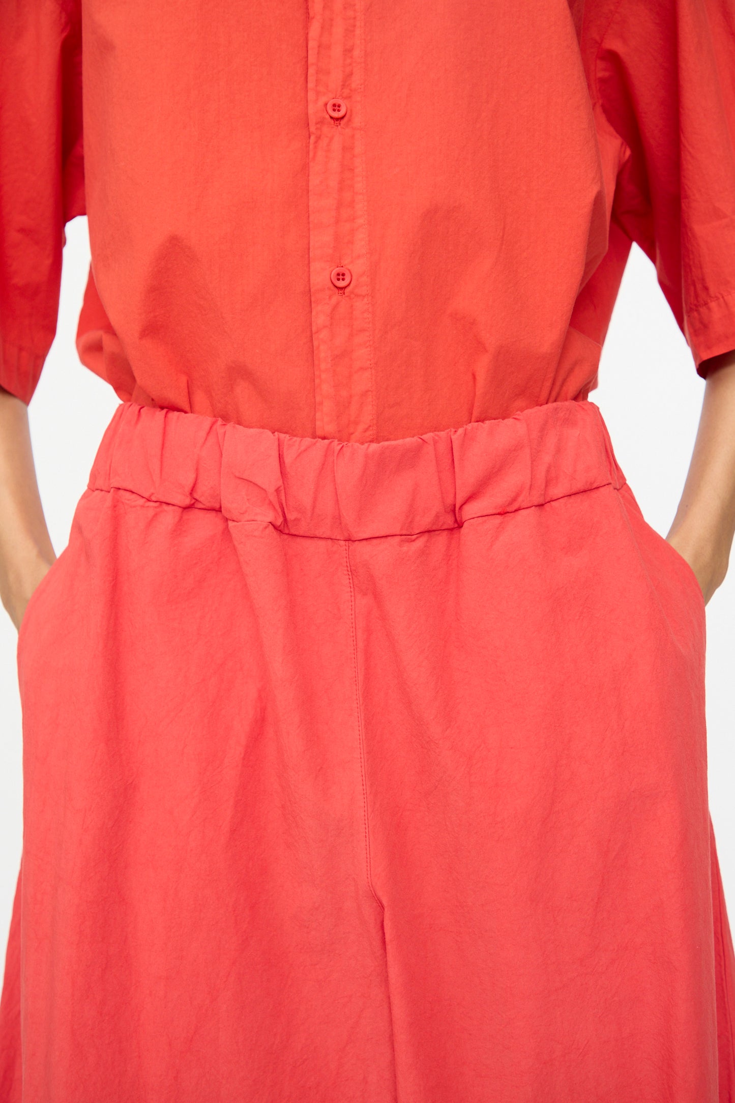 A person wears the Labo.Art Cotton Sole Pant in Tango—a high-waisted, wide-leg style paired with a loose red short-sleeve shirt. Crafted from premium cotton and made in Italy.