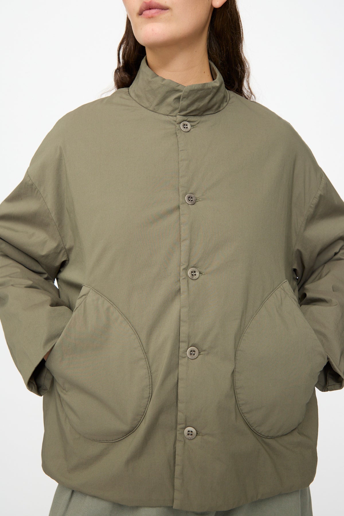 A person wearing the Labo.Art Ficus Jacket in Lichene—an olive-green, water-repellent button-up style with large front pockets—stands against a plain background.