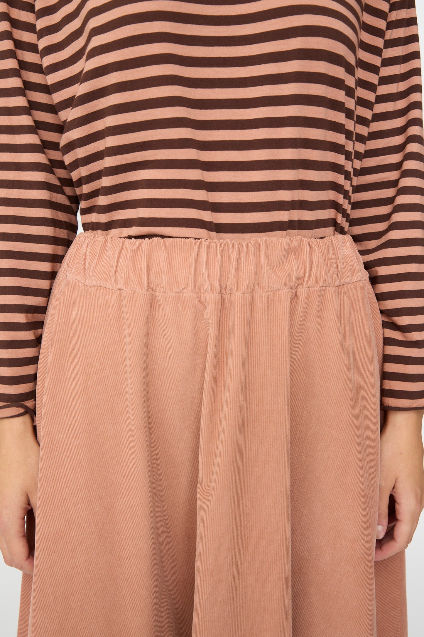 A person wearing a brown and pink striped long-sleeve top paired with the Labo.Art Gea Skirt in Canyon, a high-waisted peach A-line needlecord skirt, shown from shoulders to knees.