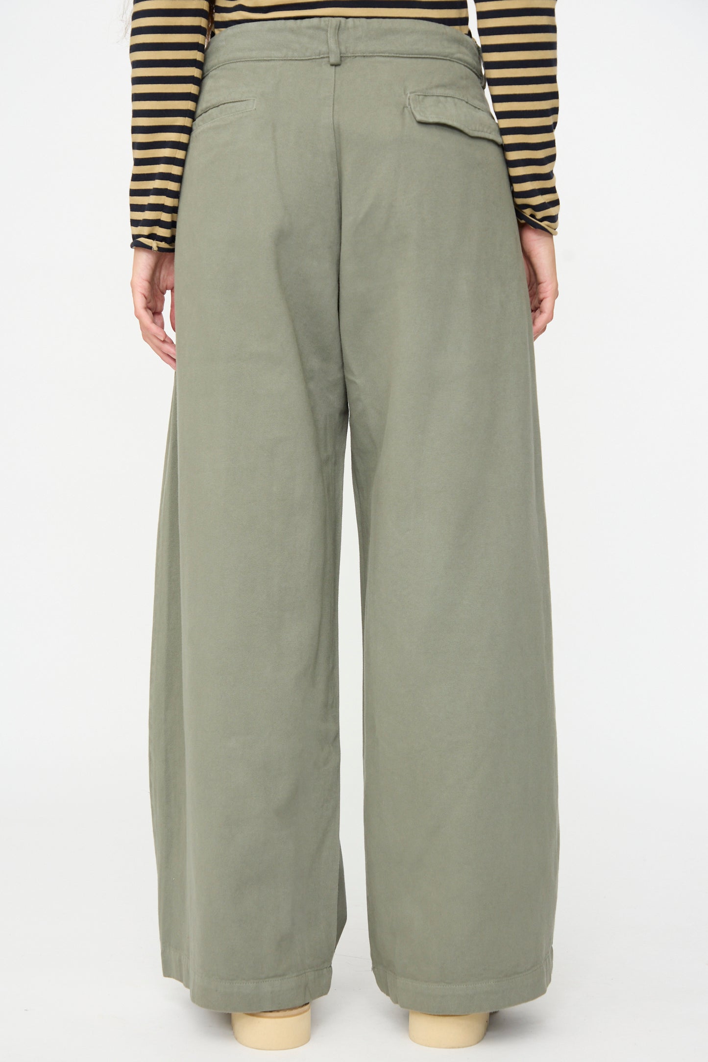 A person seen from the back against a plain white background wears the Labo.Art Marlon Trouser in Lichene—a high-waisted, wide-leg olive green brushed cotton twill pant—paired with a black and tan striped long-sleeve top.