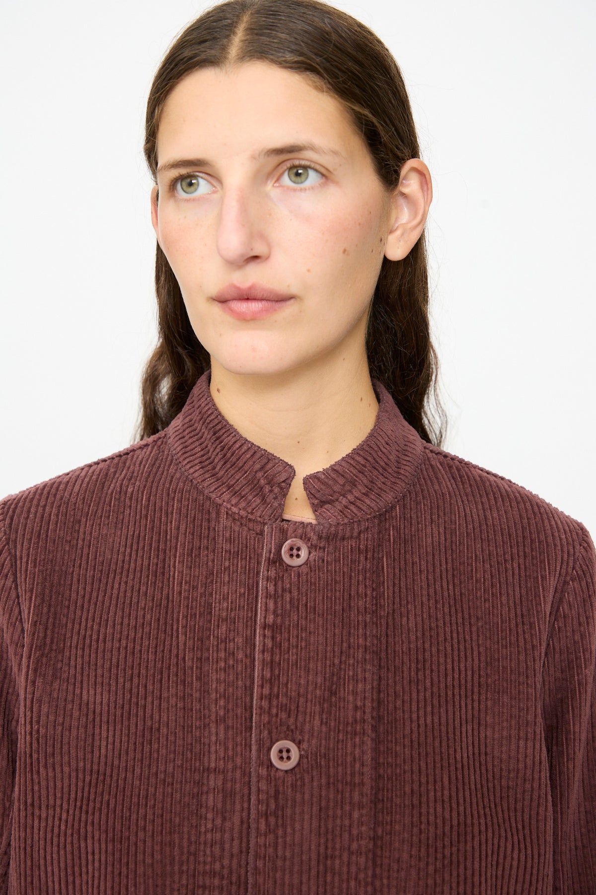 A person wearing the Labo.Art Pina Jacket in Sasso—a ribbed, maroon cotton corduroy jacket with a band collar—looks slightly to the side against a plain background.