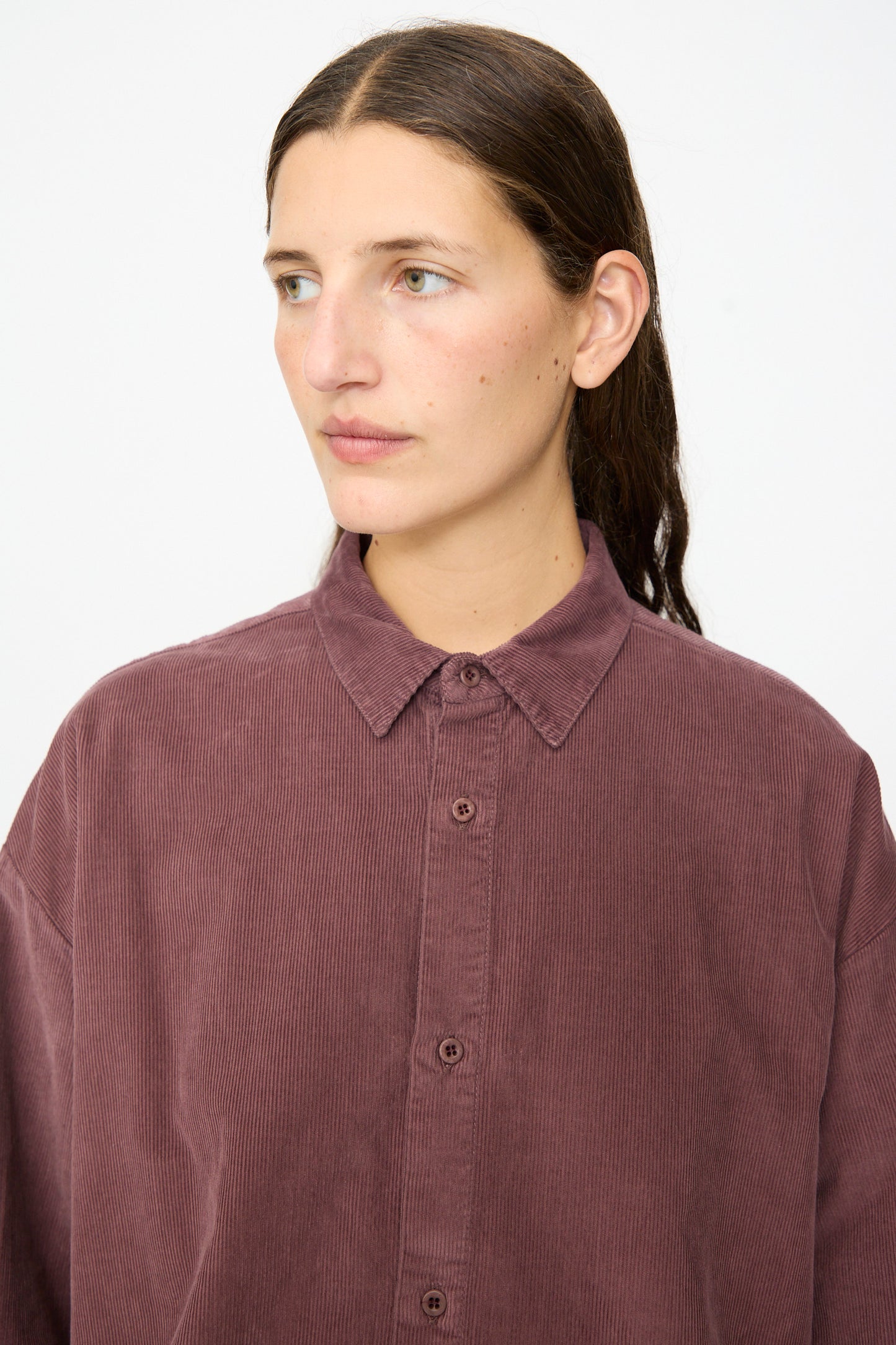 A person with straight brown hair wears the Labo.Art Quadra Shirt in Sasso—a relaxed fit, button down shirt crafted from mauve cotton needlecord—looking slightly to the left against a plain light background.